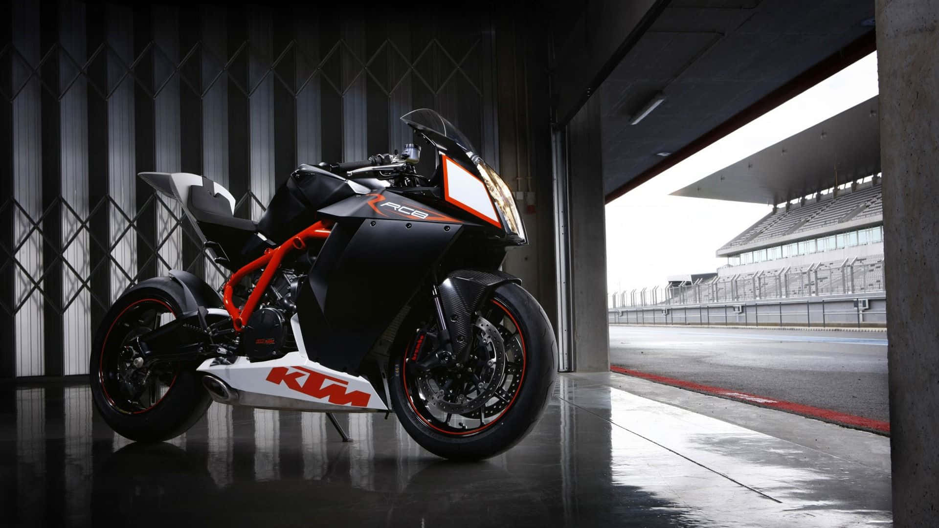 KTM 1190 RC8 圖片 壁紙 — 一架時尚的黑色和橙色KTM RC125電單車停在車庫門口，俯瞰空蕩蕩的賽道。