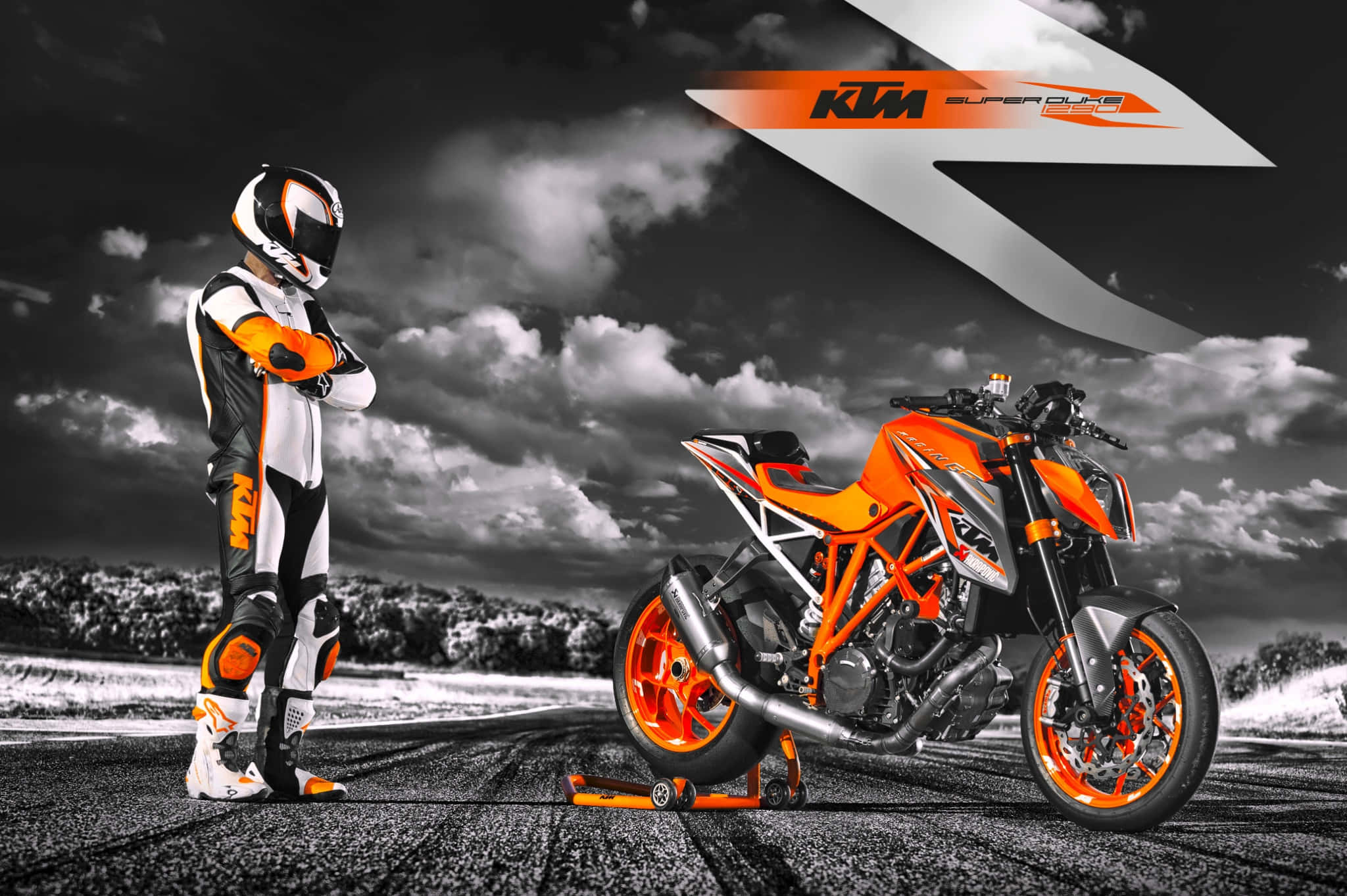 騎士駕駛KTM 1290 Duke R於賽道競速照片 壁紙 — 一名身穿全套裝備的電單車手，在戲劇性的黑白天空下，站在賽道上鮮豔的橙色KTM Super Duke電單車旁。