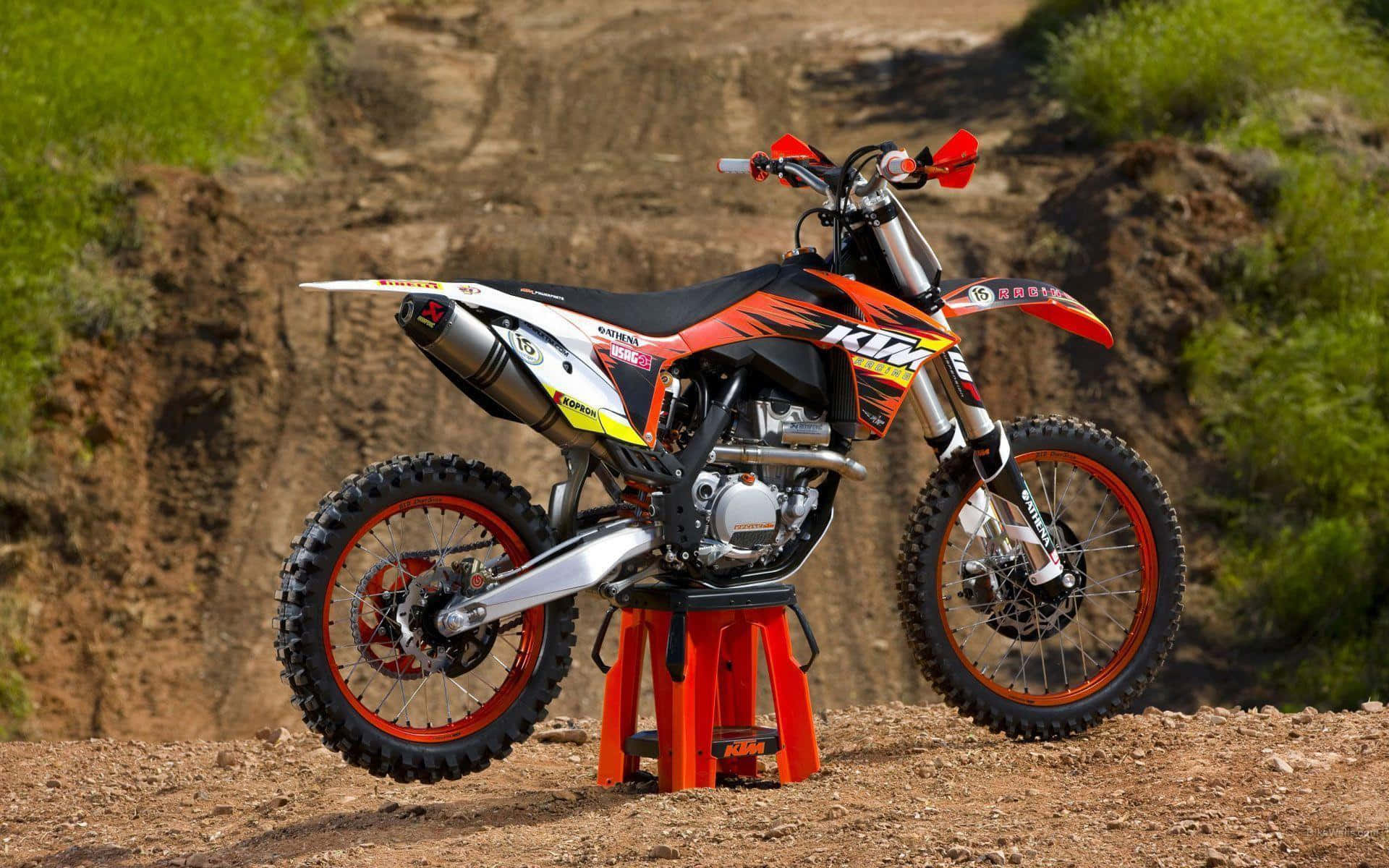 KTM 350 SX-F 圖片 壁紙 — 一架紅白色的KTM越野電單車放在橙色凳子上，位於被綠色山丘包圍的泥路上。