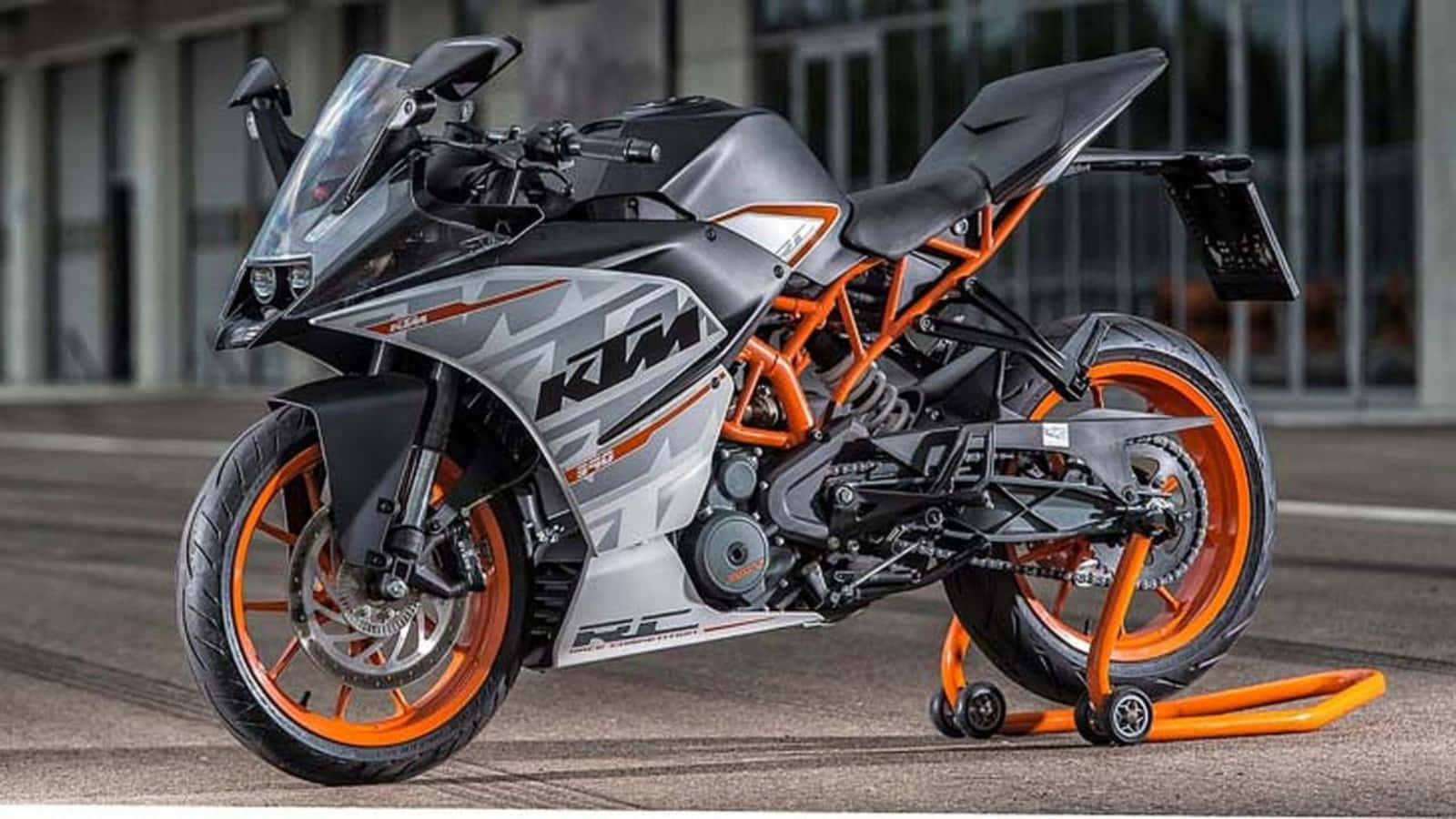 KTM 390 圖片 壁紙 — 一輛時尚的KTM RC 390電單車，帶有橙色和灰色點綴，停在鋪砌路面上的亮橙色支架上。