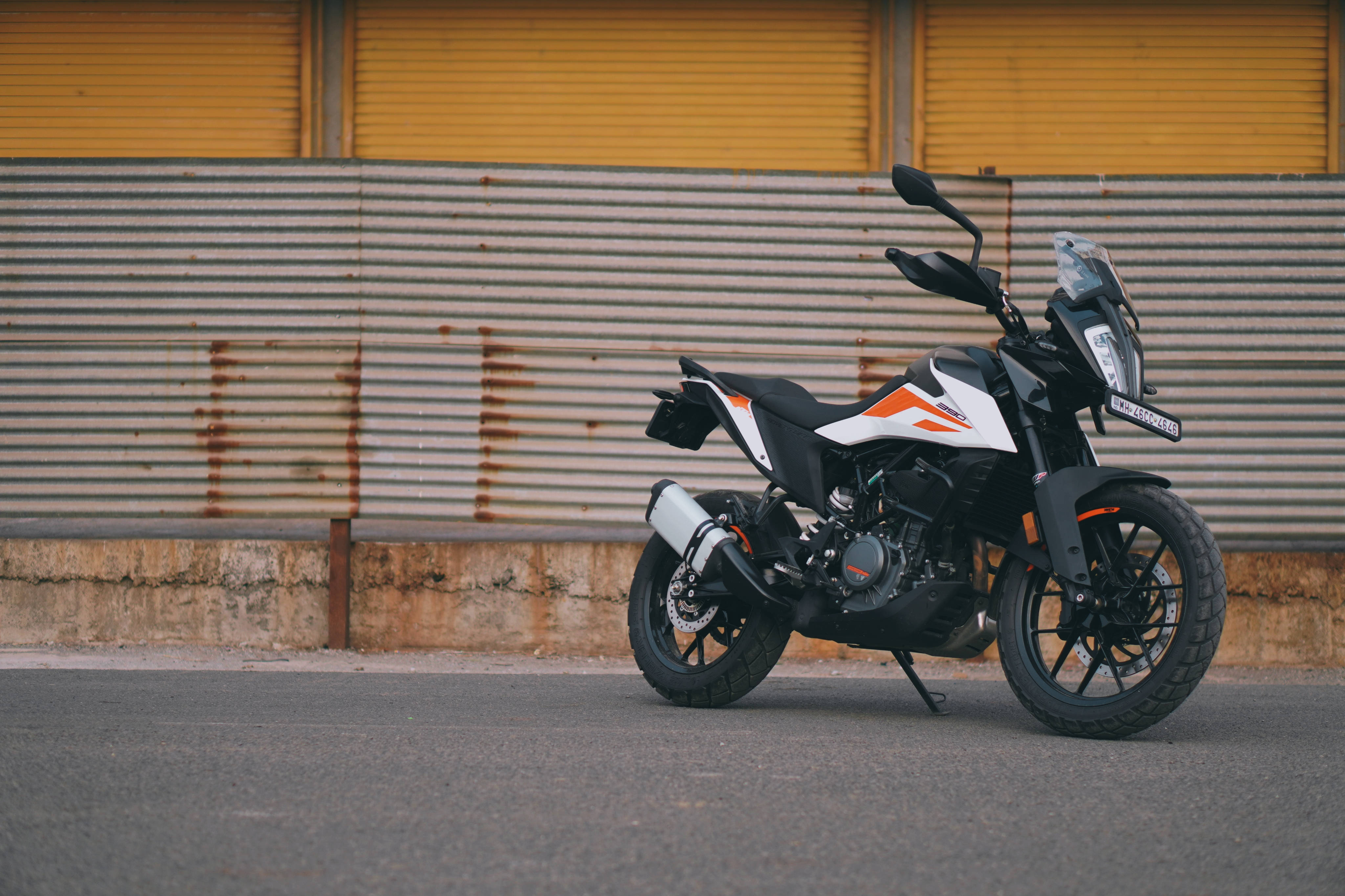 KTM 390 Duke停在柏油路上 壁紙 — 一輛黑色和橙色的冒險電單車停在瀝青路上，背景是帶有鏽跡的風化波紋金屬牆。