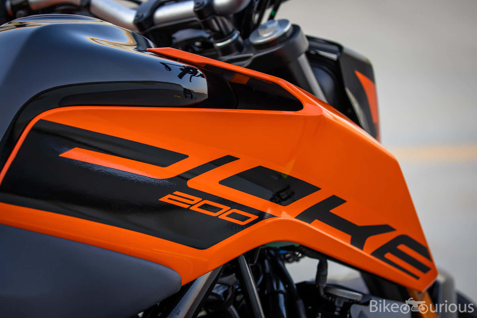 KTM Duke 200 機車圖片 壁紙 — KTM 200電單車油箱特寫，鮮豔橙色與黑色，光面處理，品牌標誌突出。