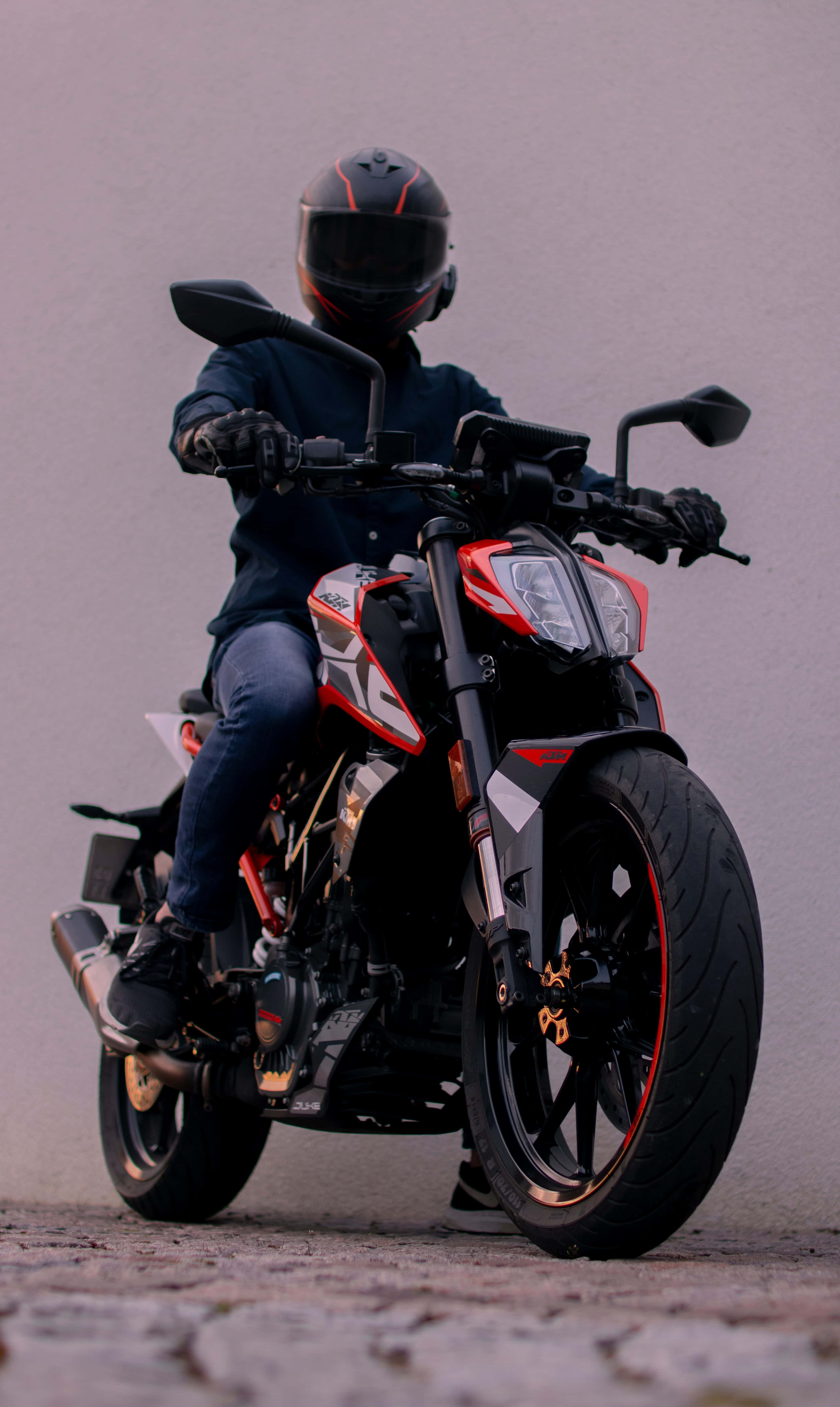 騎士駕馭黑紅配色KTM Duke 390 壁紙 — 一名戴著黑色頭盔的騎士坐在紅色和黑色的運動摩托車上，背景是柔和的灰色。