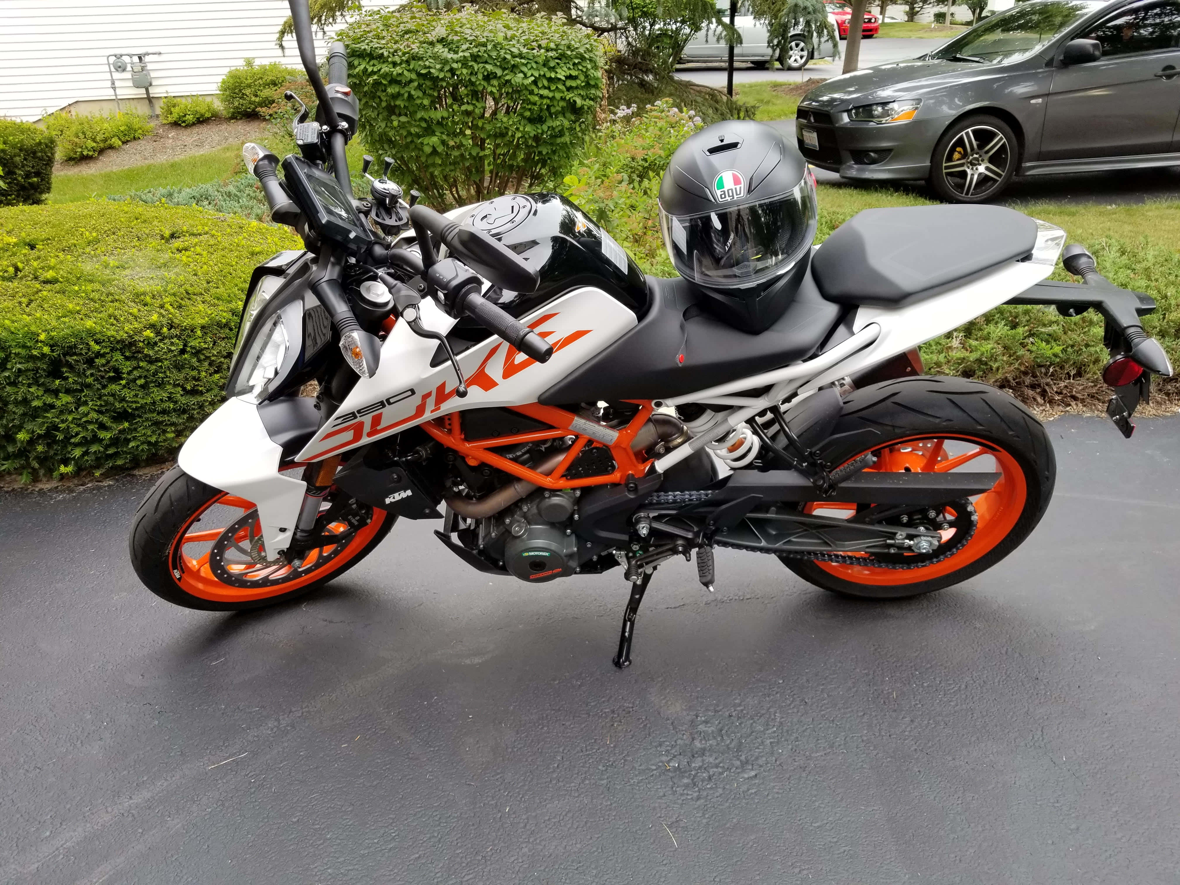 KTM Duke 390摩托車配頭盔照片 壁紙 — 一輛白色和橙色的KTM 390 Duke電單車停在濕漉漉的路面上，座位上放著一個頭盔。