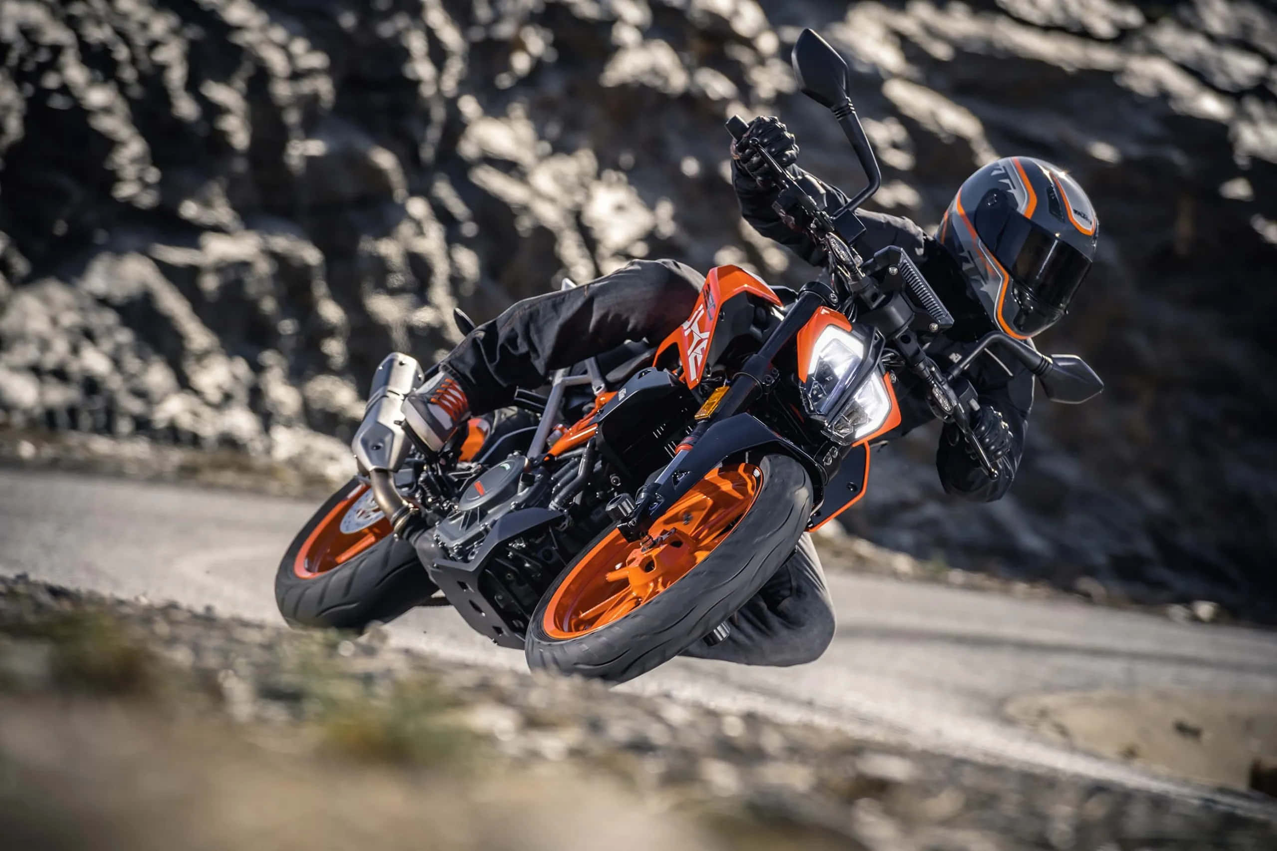 騎乘KTM Duke 390，感受脈搏中奔騰的刺激 壁紙 — 一名騎士在岩石山路上方凌空騎著橙色KTM電單車傾身進入急彎。