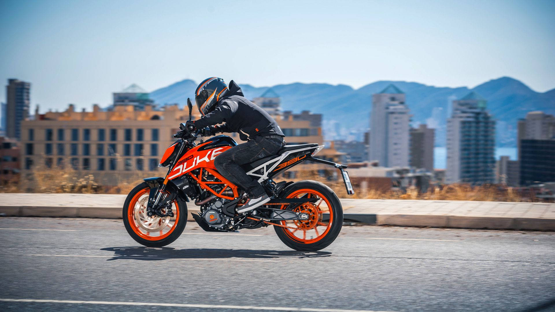 電單車手騎橙色KTM Duke在城巿道路上，背景有山巒