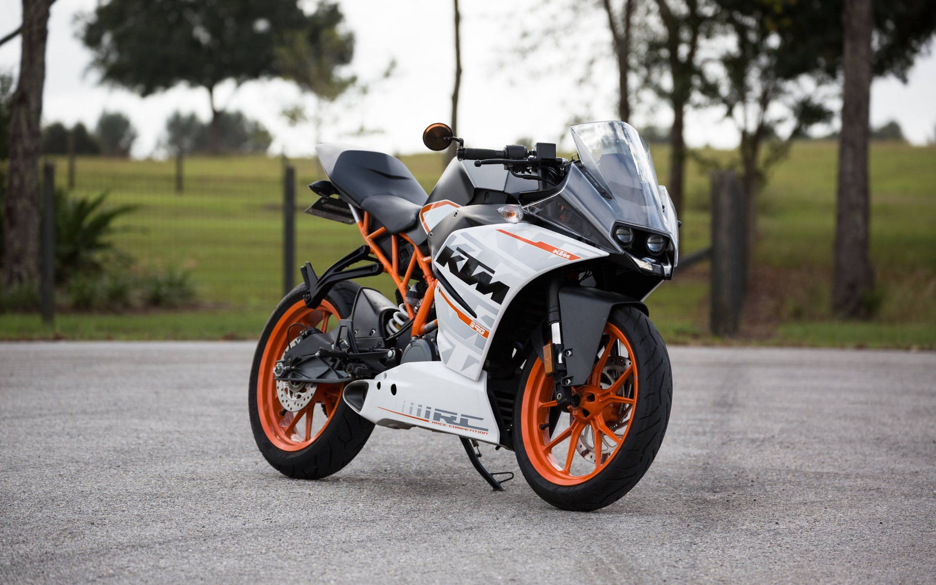 白色和橙色KTM RC電單車停在鋪砌道路旁，靠近樹木。
