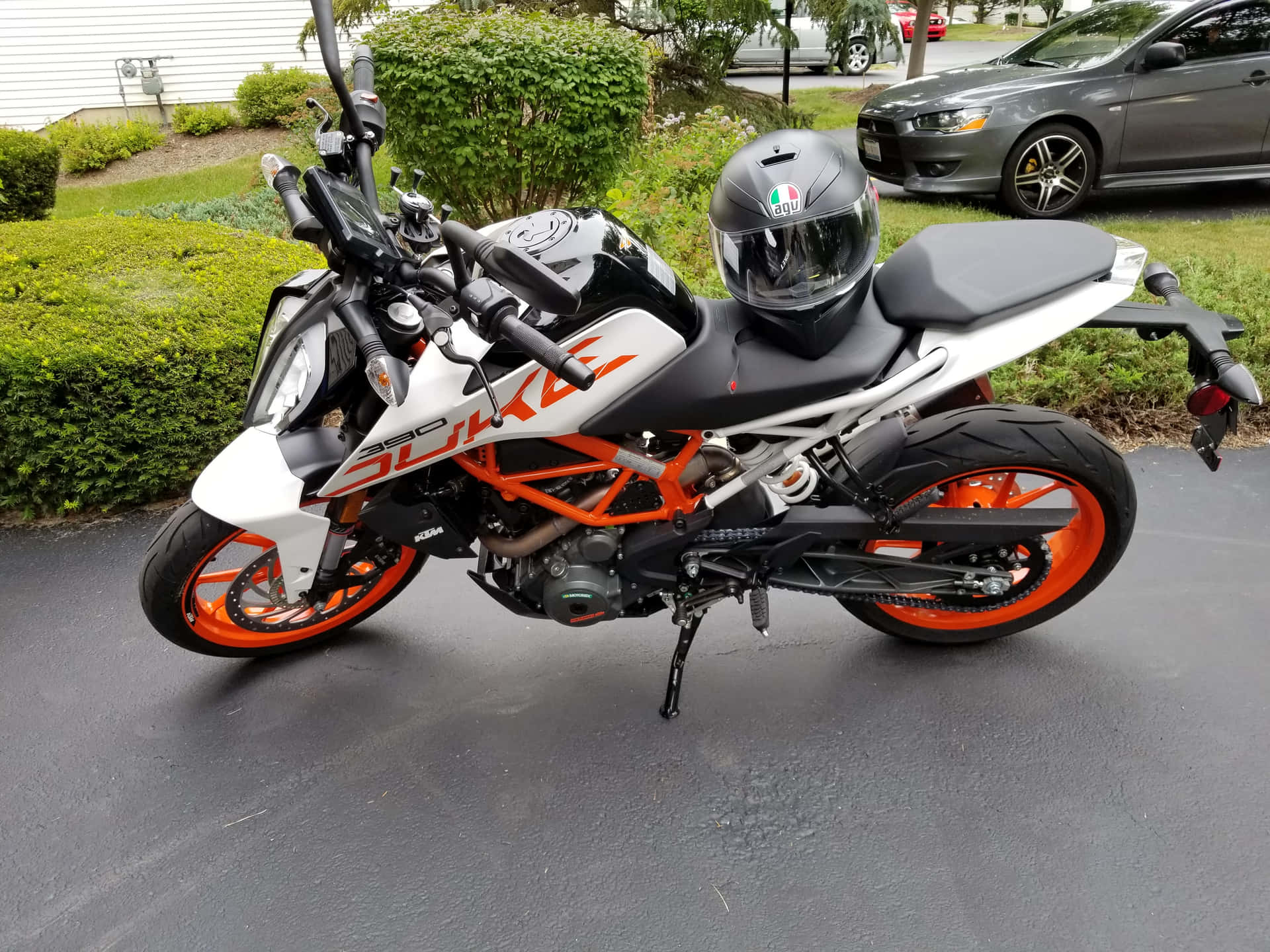 白色和橙色的KTM 390 Duke電單車停在濕路面上，座位上有頭盔。