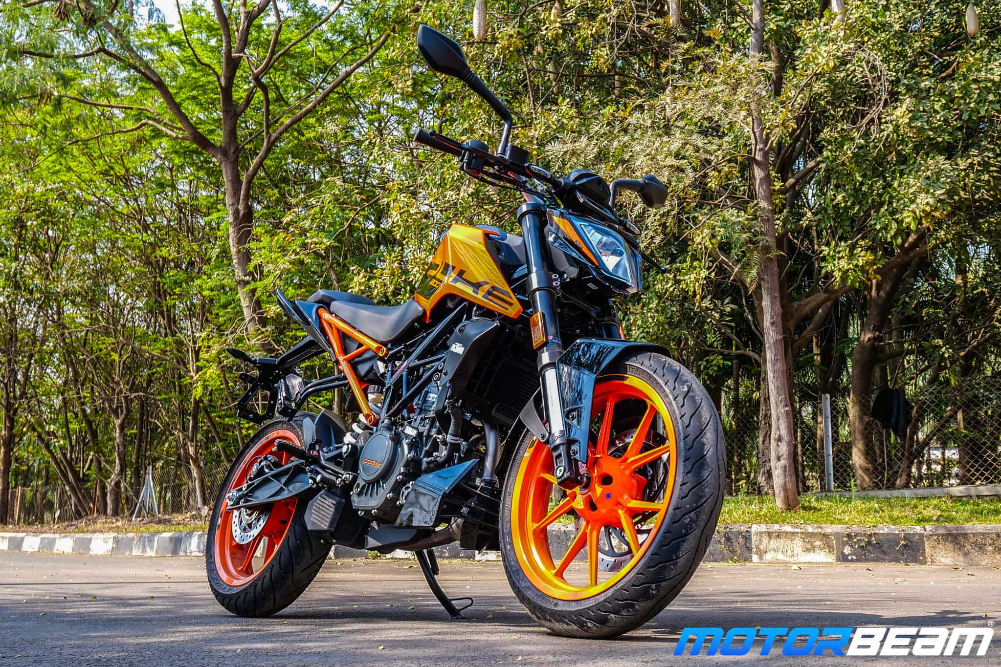 街頭停泊的KTM Duke摩托車 壁紙 — 一架鮮豔的橙色和黑色KTM電單車停泊在樹蔭大道上，在明亮的日光下。