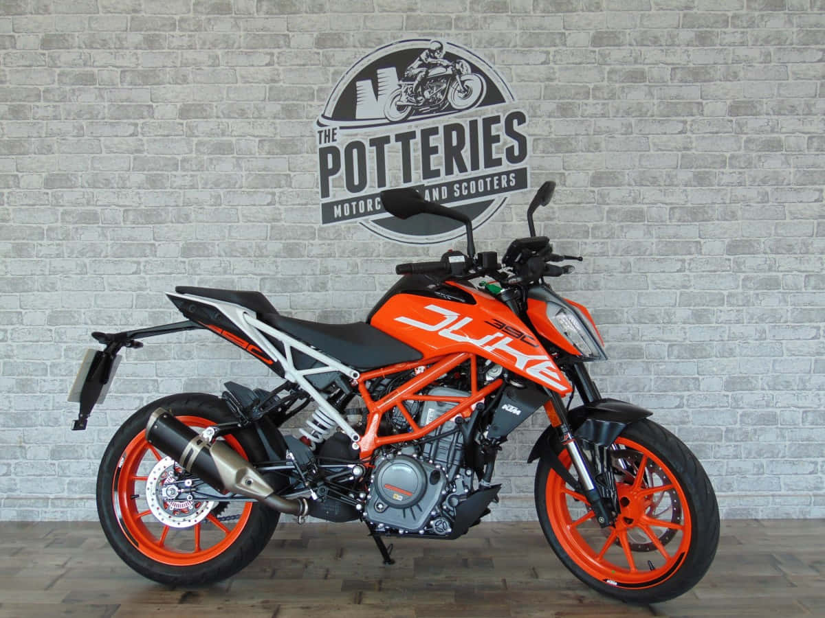 KTM Duke摩托車 - 出發吧！ 壁紙 — 鮮豔橙色KTM Duke電單車停放在室內，背景是帶有經銷商標誌的灰色磚牆。