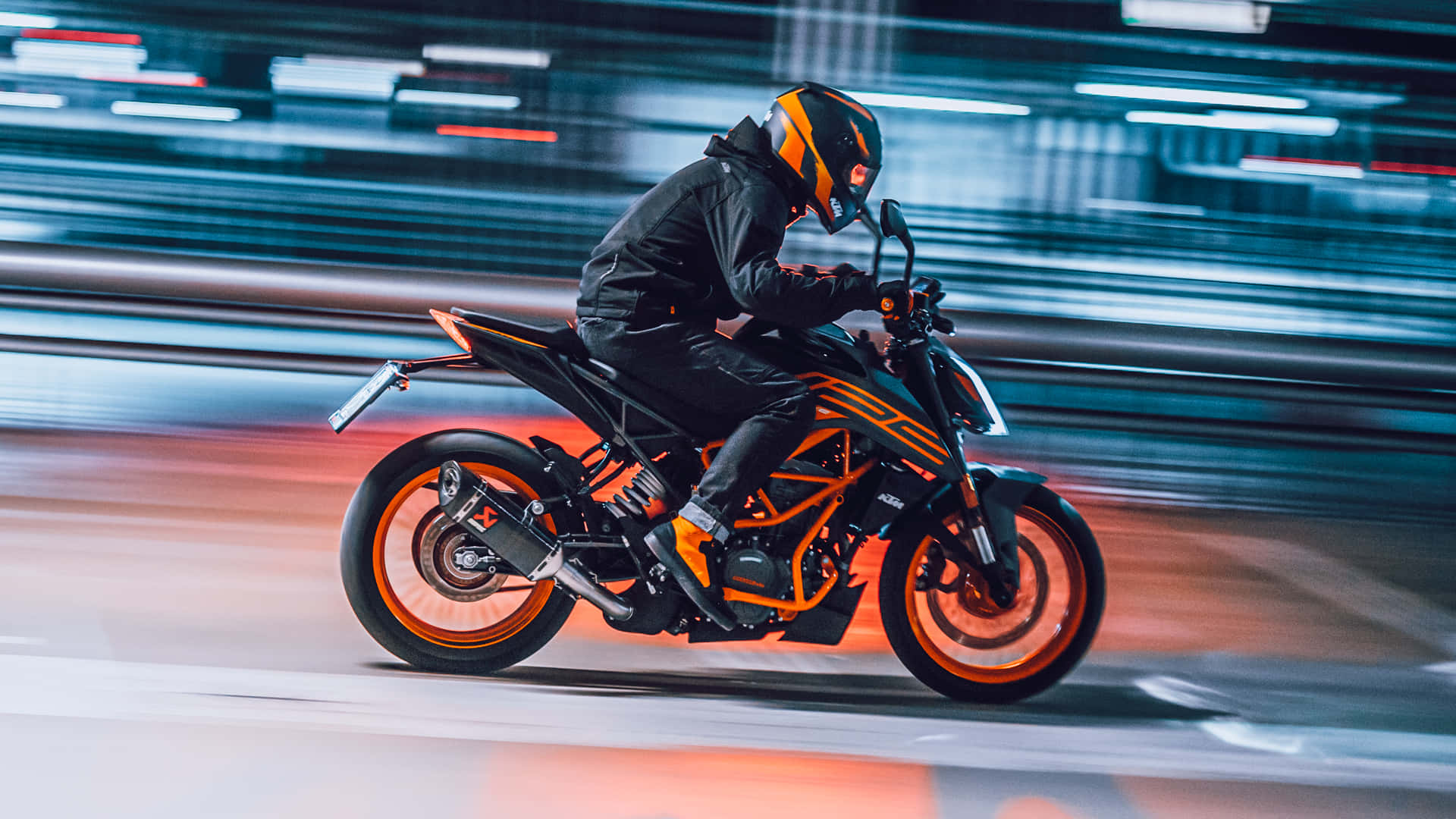 夜間騎乘KTM Duke的動感模糊畫面 壁紙 — 一名身穿黑色和橙色裝備的電單車手，在霓虹燈閃爍的都市夜晚高速飛馳，身後留下光跡。