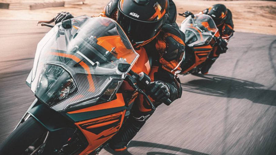 兩輛 KTM RC 200 賽道競速 壁紙 — 兩名身穿橙色和黑色裝備的車手，在陽光明媚的賽道上騎著高性能KTM電單車傾斜入彎。
