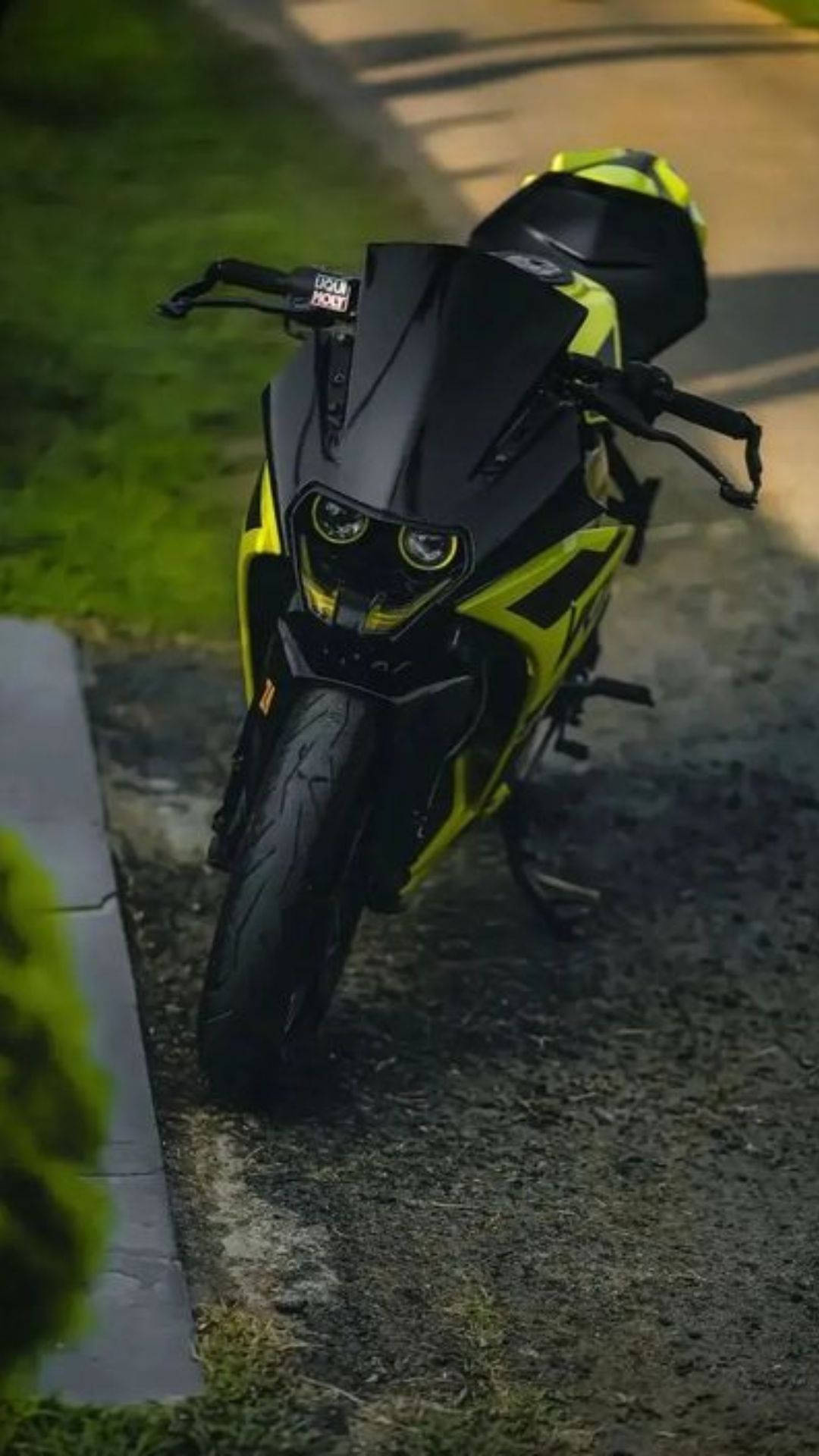 黑綠配色KTM RC 200 壁紙 — 一架時尚的黑色和螢光黃色運動電單車在黃昏時停泊在碎石路上，旁邊是綠草。