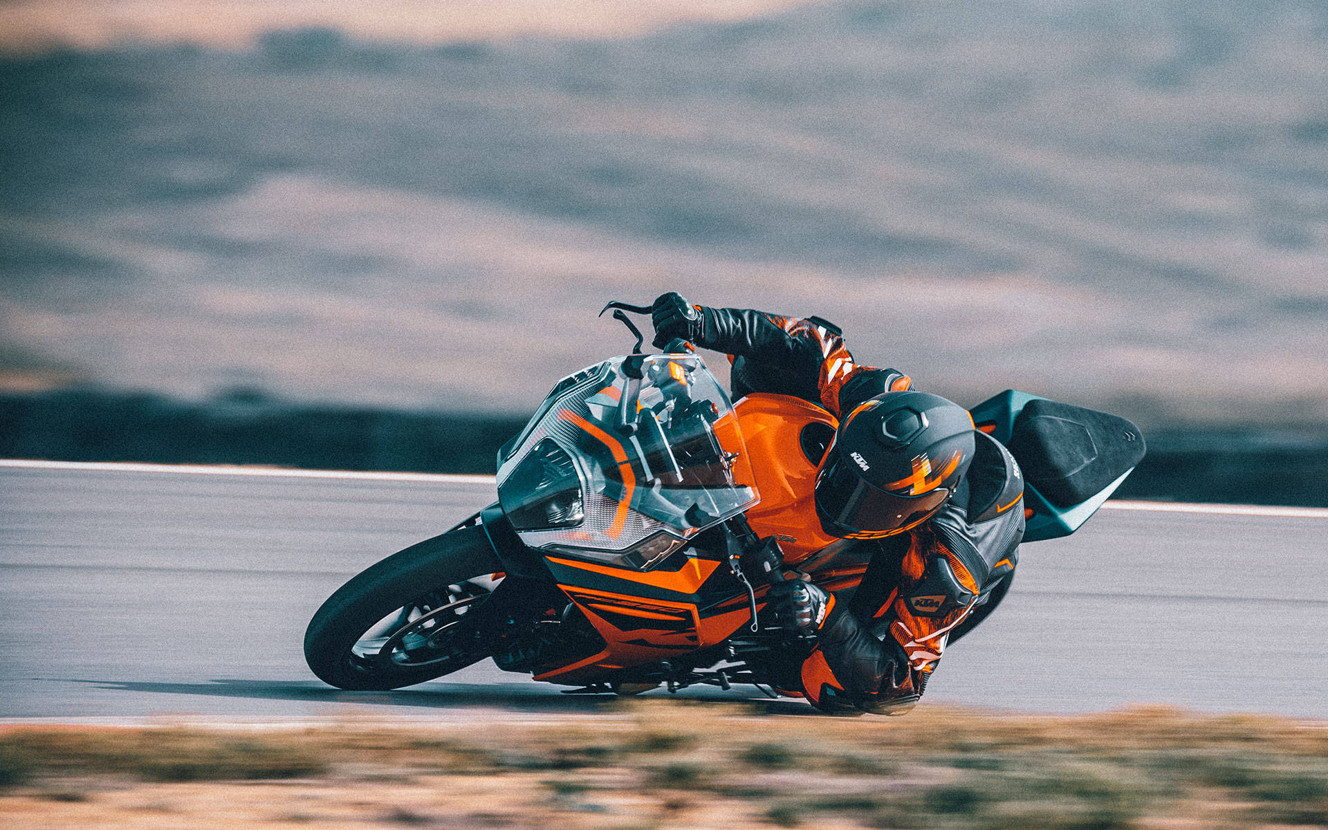 KTM RC 200 緊急彎道 壁紙 — 一名身穿橙色裝備的車手在陰天下的賽道上，騎著一輛鮮橙色運動電單車傾斜入急彎。