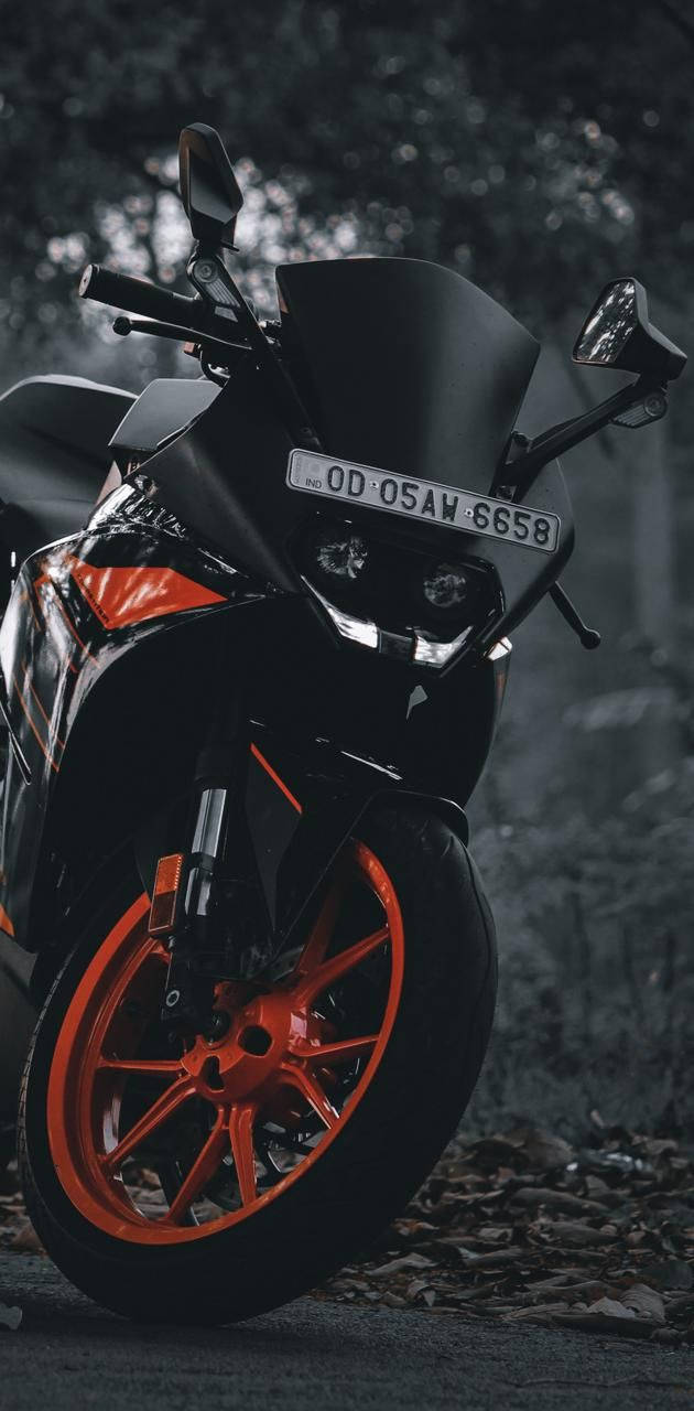 黑色KTM RC 200近距離特寫 壁紙 — 一架時尚黑色運動電單車配以鮮豔橙色輪胎，停泊在樹葉茂密的森林小徑上，燈光營造出氣氛。
