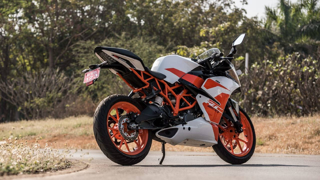 沙漠路中停泊的 KTM RC 200 壁紙 — 一輛白色和橙色的KTM電單車停泊在鋪砌的道路上，背景有乾草和樹木。