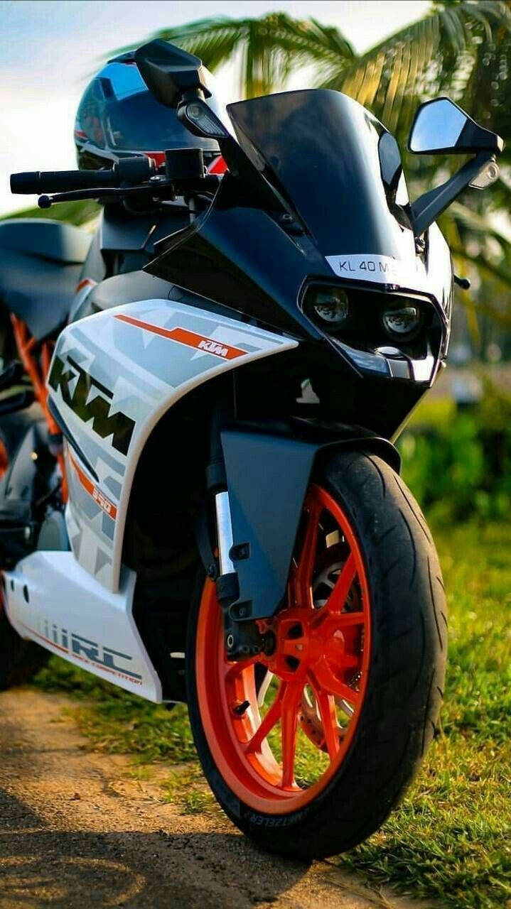 白色KTM RC 200 壁紙 — 一架時尚的黑白KTM電單車，配以鮮豔的橙色輪胎，停泊在棕櫚樹下的草地上。
