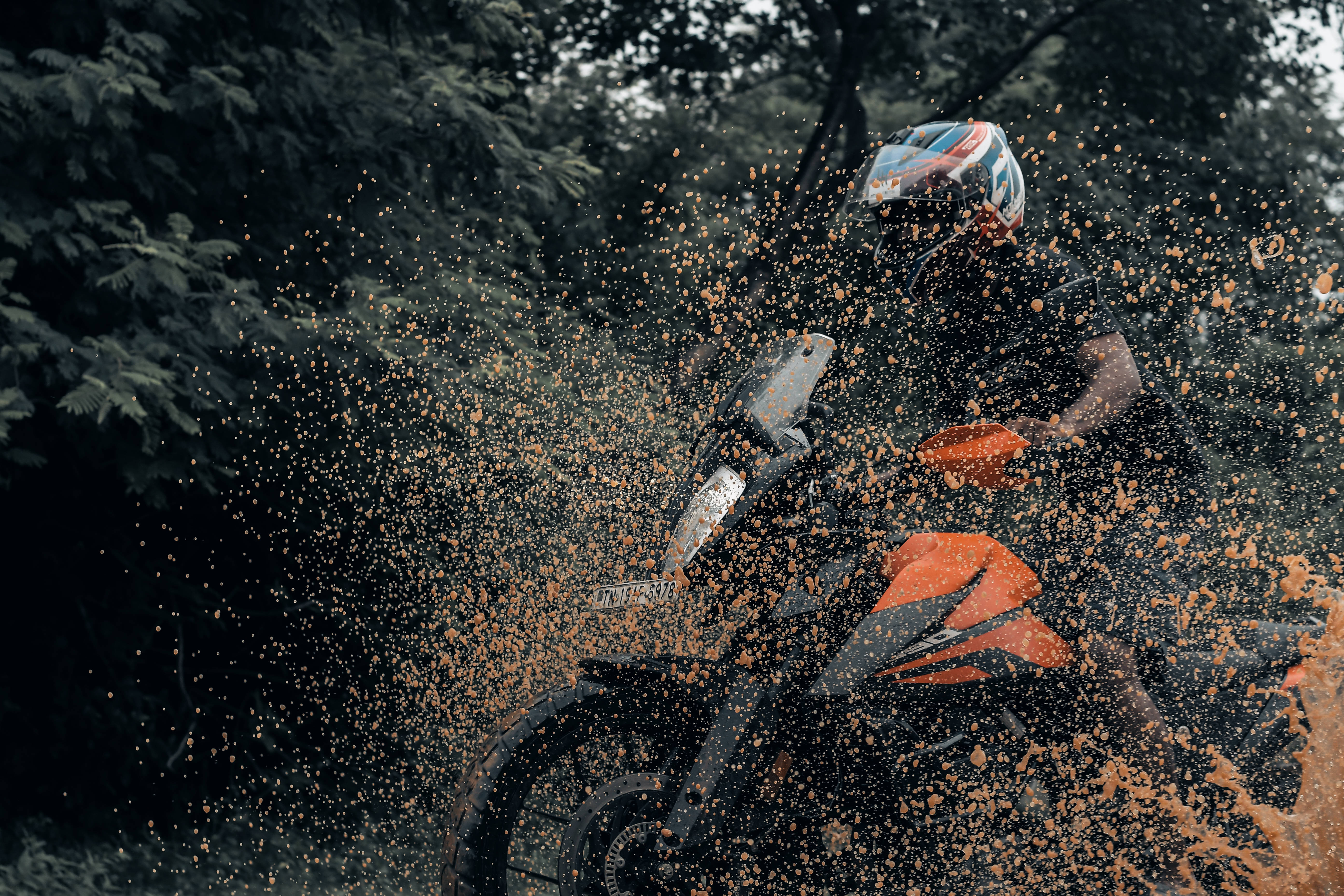 KTM RC 390 泥濘路 壁紙 — 一名電單車手戴著色彩繽紛的頭盔，在森林地區的泥濘地形上行駛，濺起橙色的水花。