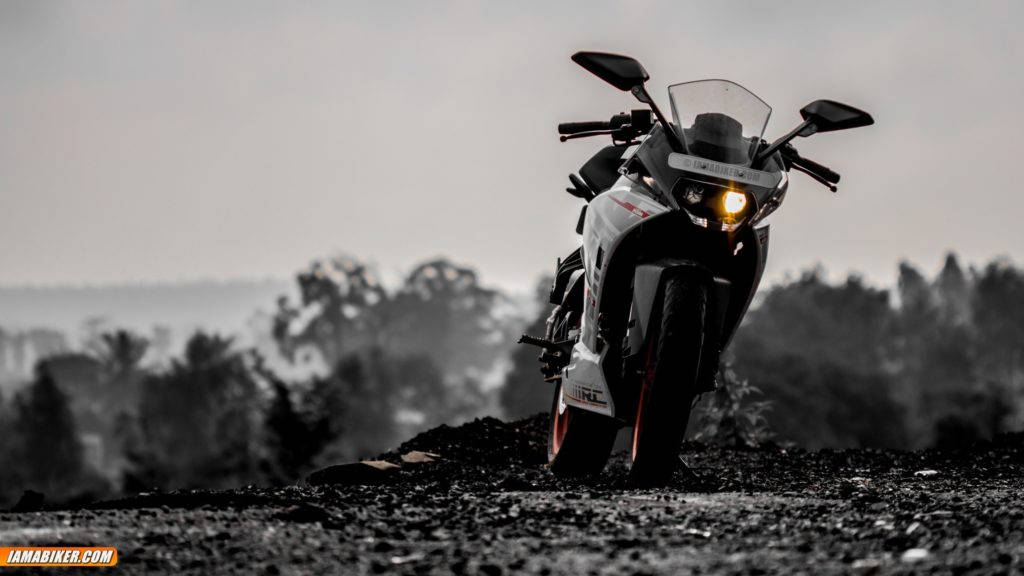 KTM RC 390正面視角 壁紙 — 一輛帶有發光頭燈的運動電單車，佇立在碎石山丘上，背景是朦朧的黑白風景。
