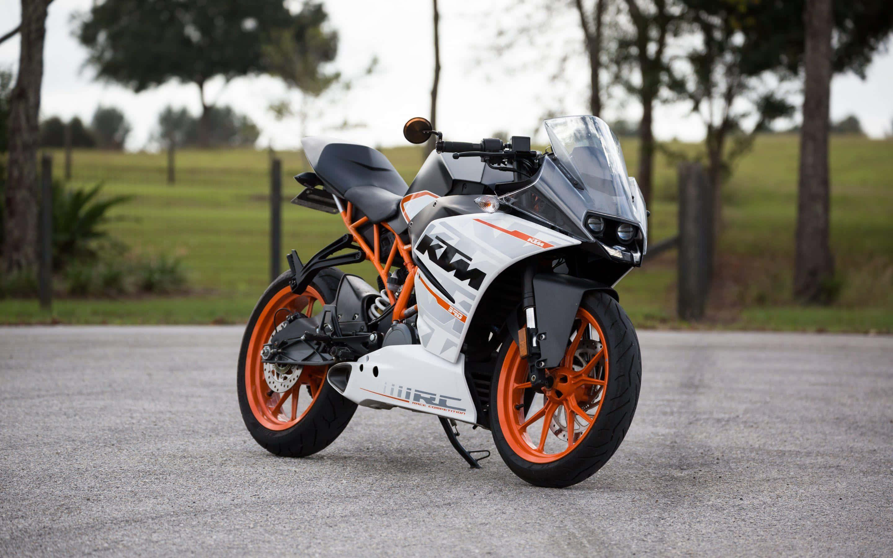 KTM RC8R圖片 壁紙 — 一架白色和橙色嘅KTM RC電單車，型格咁停泊喺碎石路上，背景有樹木同草地。