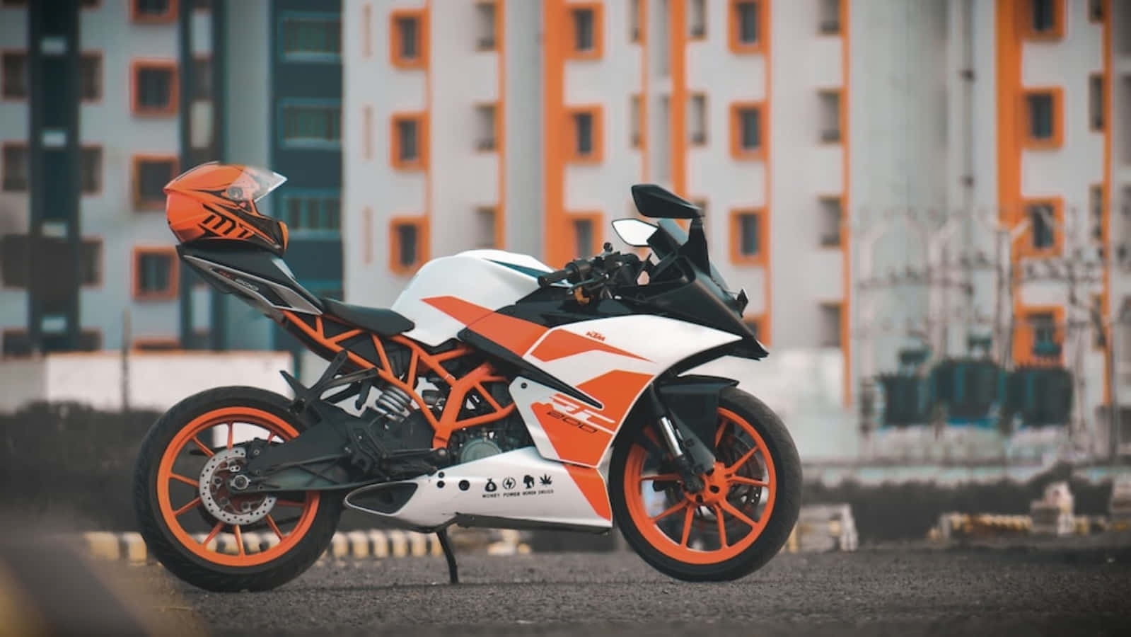 KTM RC照片 壁紙 — 一架時尚的橙色和白色KTM運動電單車停泊在瀝青路上，背景是現代建築。