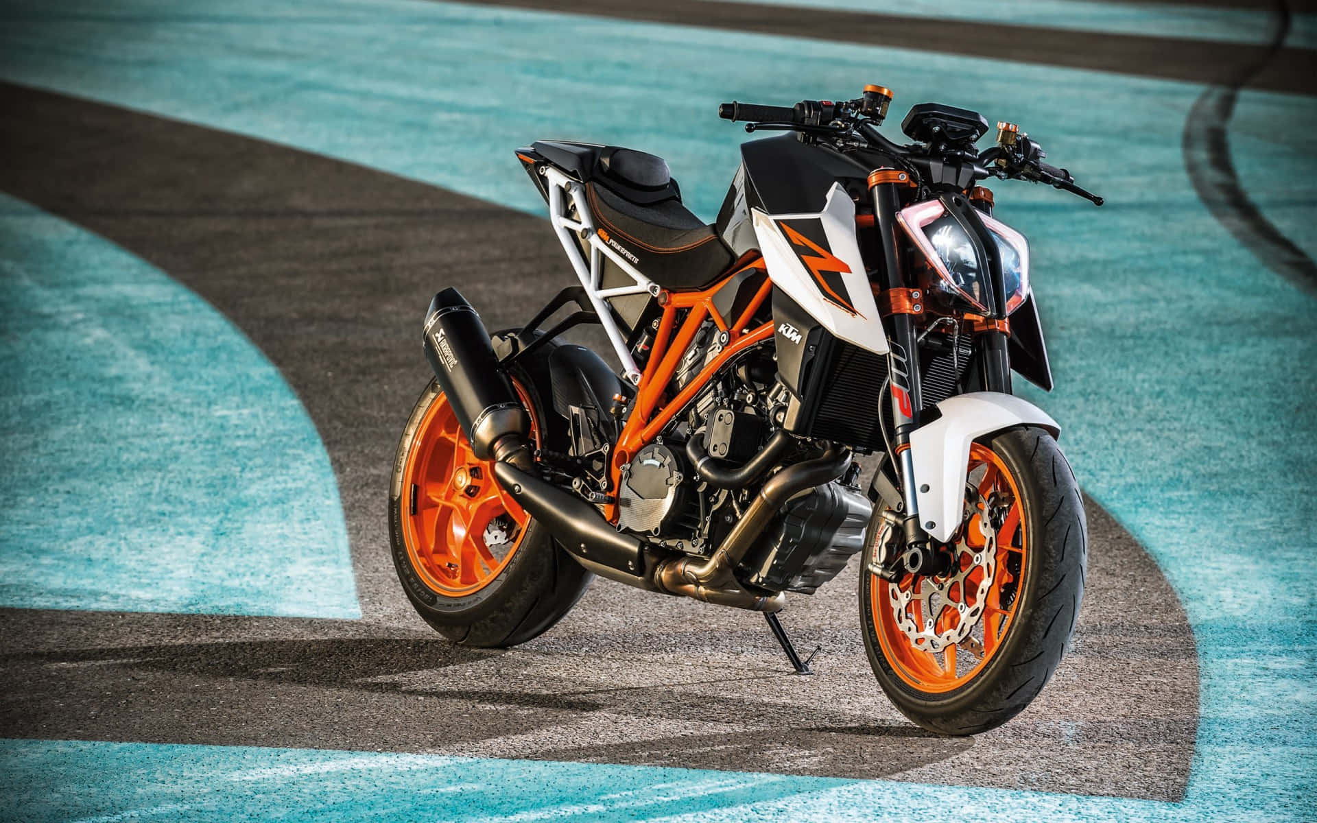 KTM Super Duke 圖片 壁紙 — 一輛時尚的橙色和白色KTM電單車停在彎曲的賽道上，賽道鋪有充滿活力的藍色瀝青。