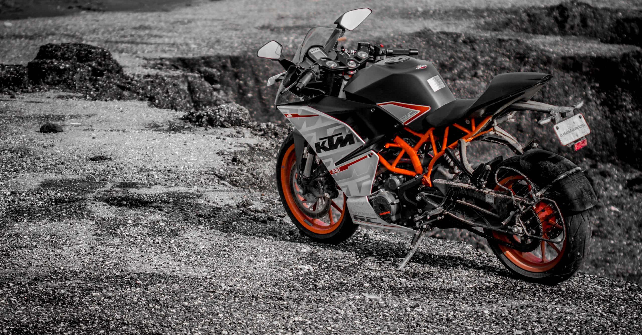 KTM 機車停於碎石小徑 壁紙 — 一輛醒目的橙色和黑色KTM電單車獨自停在碎石地面上，背景飽和度降低。