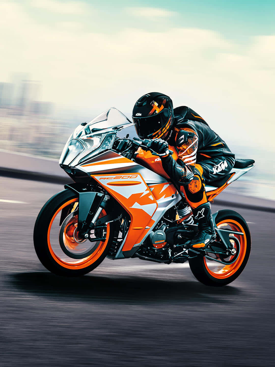 KTM賽道照片 壁紙 — 一名身穿黑色和橙色裝備的騎士在KTM RC 200電單車上傾斜入彎，城市道路上帶有動態模糊效果。