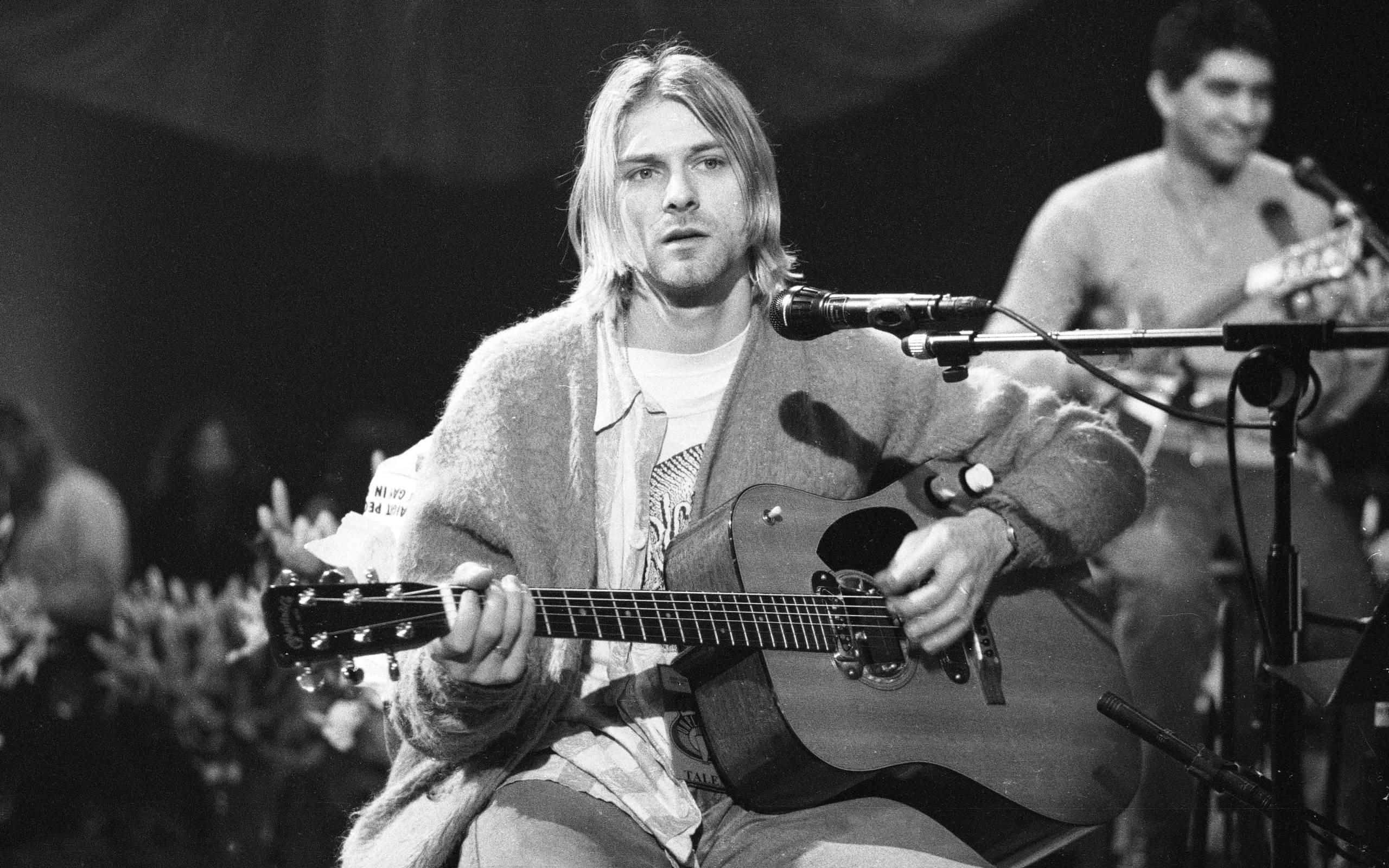 nirvana 桌布 壁紙 — Kurt Cobain 在舞台上彈奏木結他，黑白影像，在舞台燈光下展現高度專注。