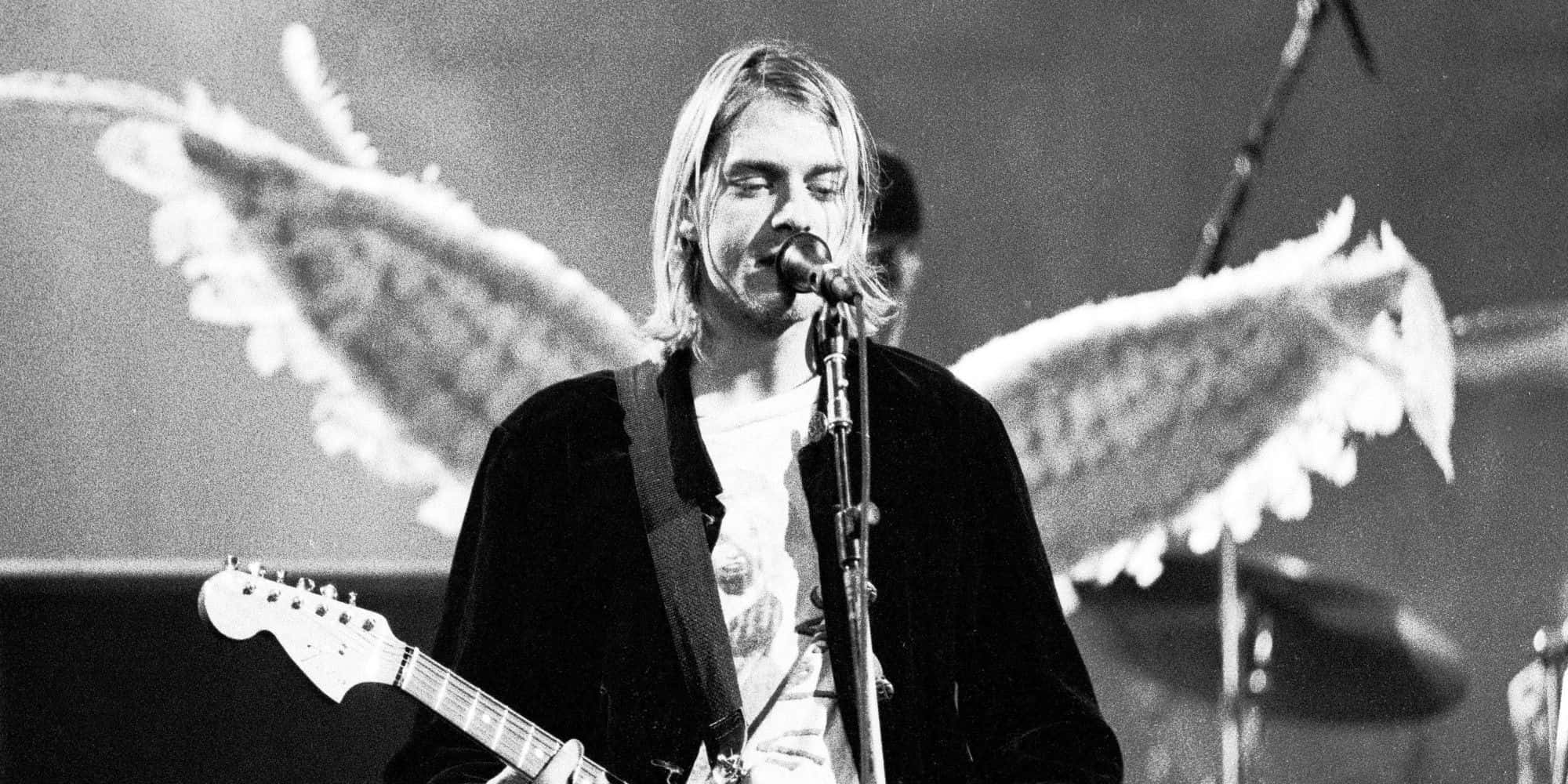 涅槃 桌布 壁紙 — Kurt Cobain 在黑白照片中，身後有天使翅膀，在舞台上表演。