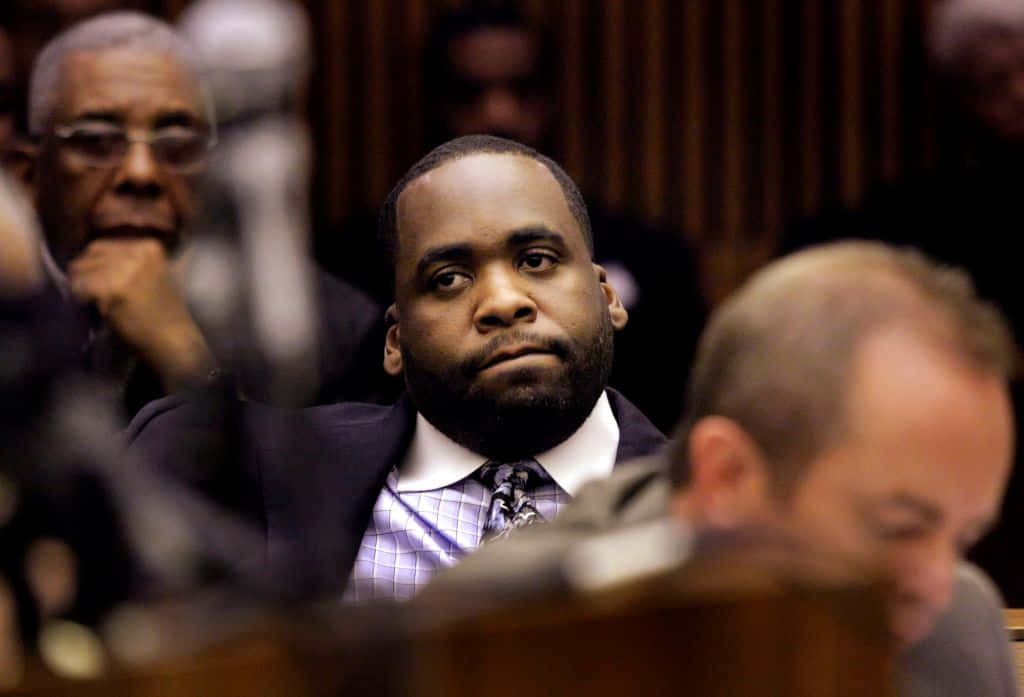 前底特律市長Kwame Kilpatrick於公開活動發言 壁紙 — 一位穿著西裝打領帶的莊嚴男子坐在法庭內，周圍有模糊的人物。