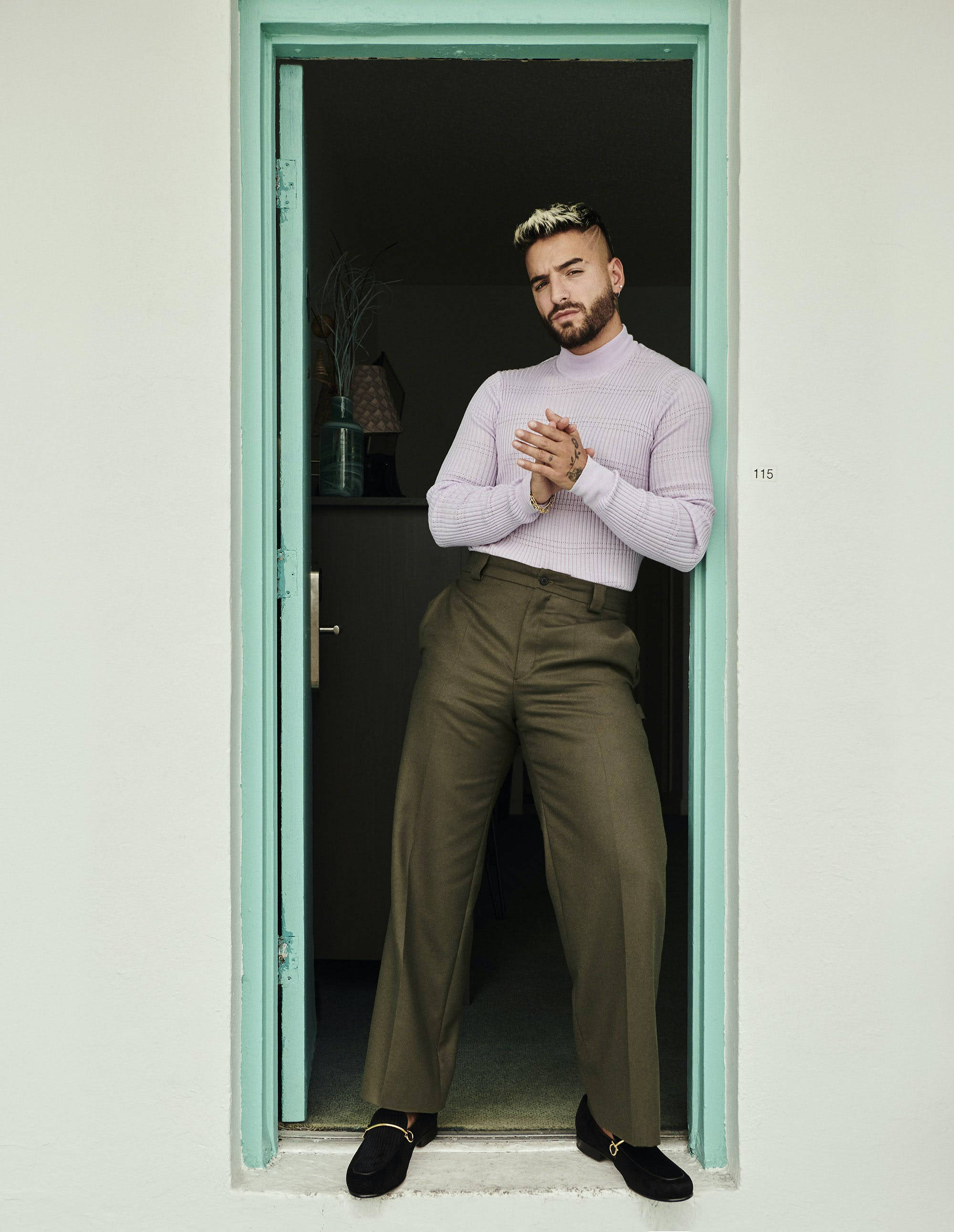 馬盧馬 L'Officiel Hommes 壁紙 — 一位留鬍子、金髮的時尚男士站在薄荷綠色的門口，穿著薰衣草色高領毛衣和橄欖色褲子。