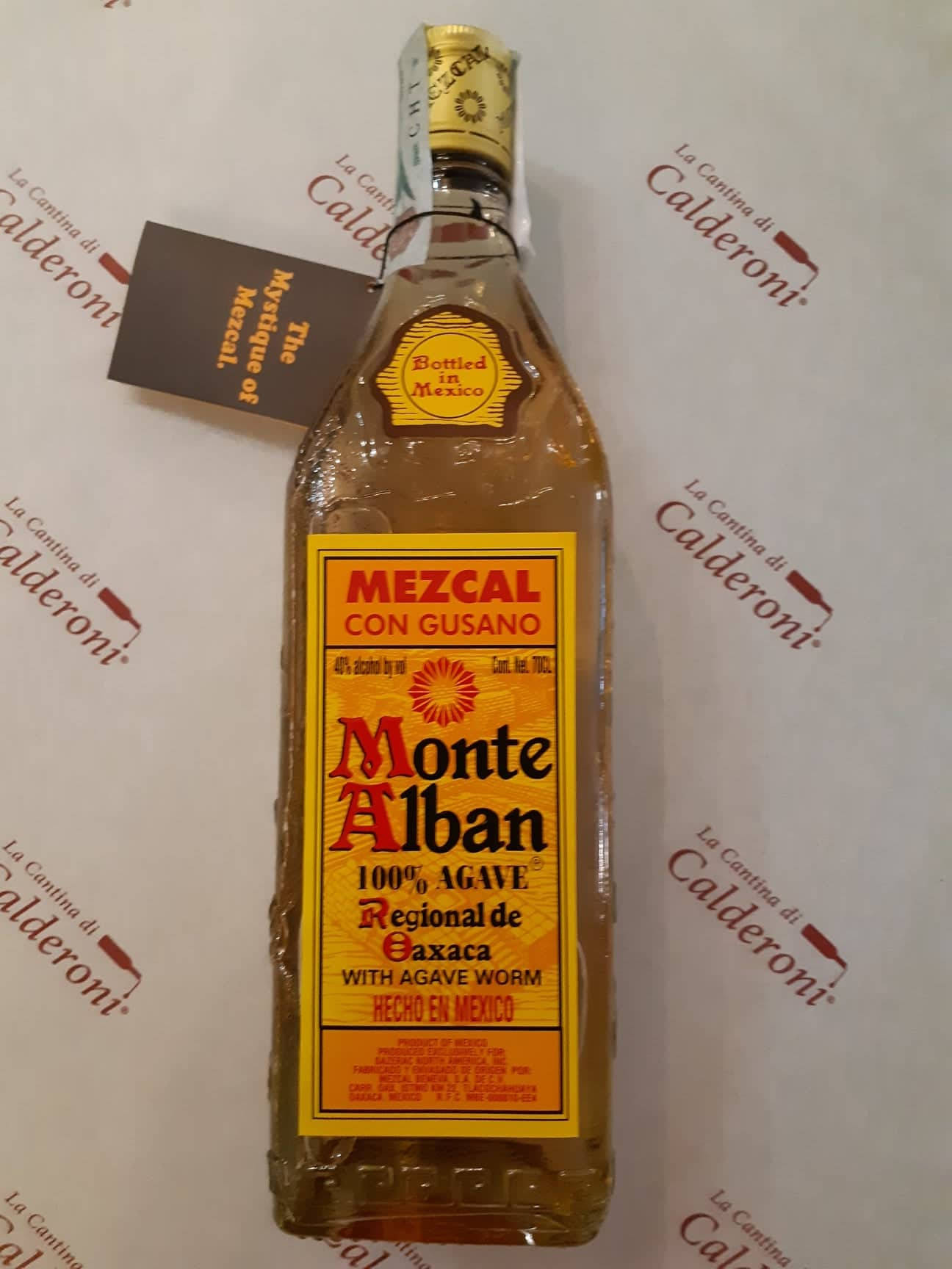 一瓶有龍舌蘭蟲的 Monte Alban 梅斯卡爾酒，放在有品牌標誌的紙上。