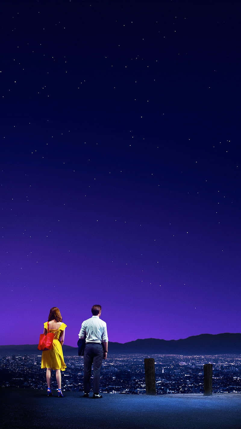 擁抱La La Land的魔力 壁紙 — 一對情侶站在山丘上，俯瞰著廣闊星空下閃耀的城市。