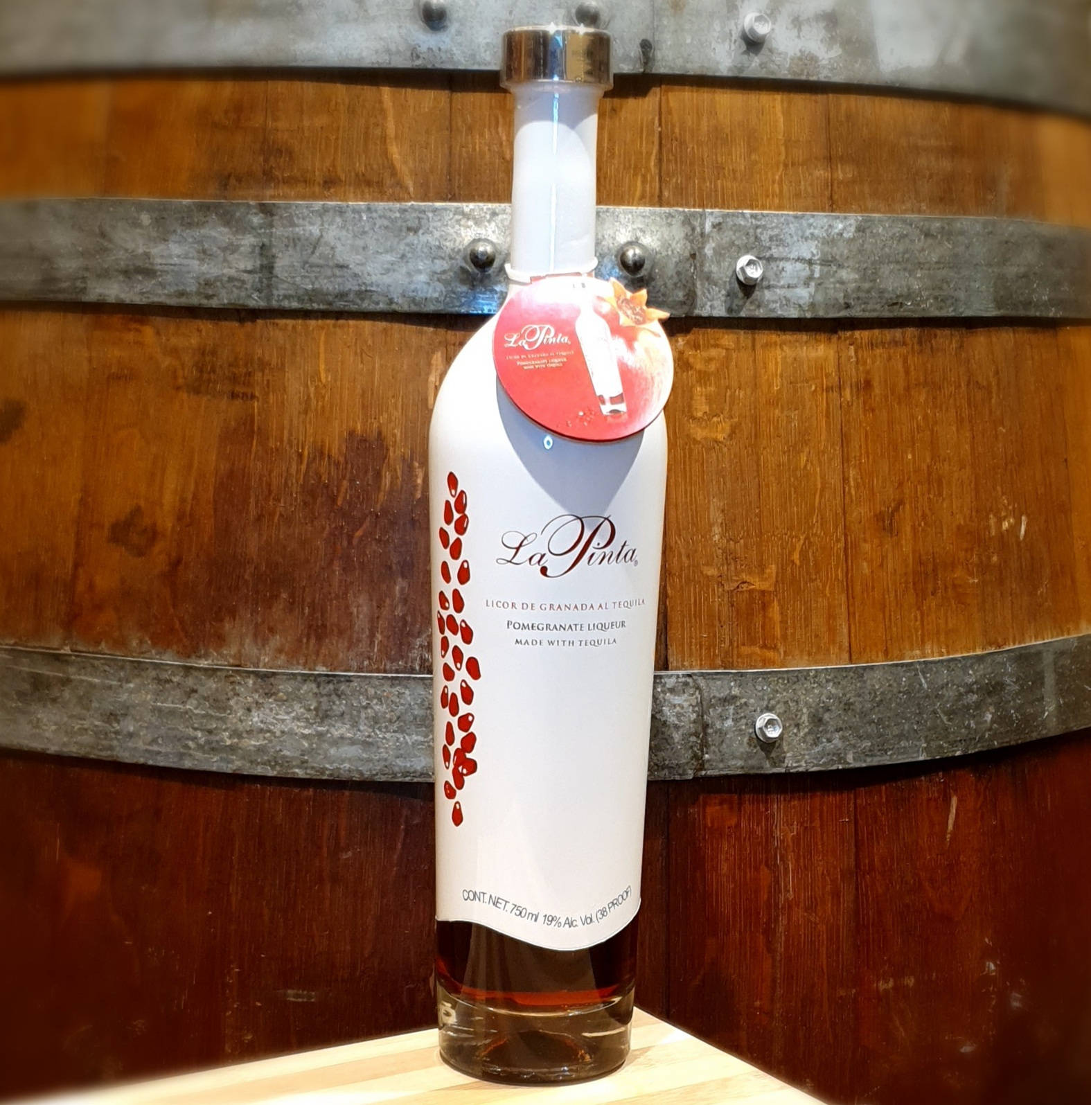 La Pinta石榴 liqueur 壁紙 — 一瓶白色La Pinta石榴利口酒放在木質表面上，背景是質樸的葡萄酒桶。