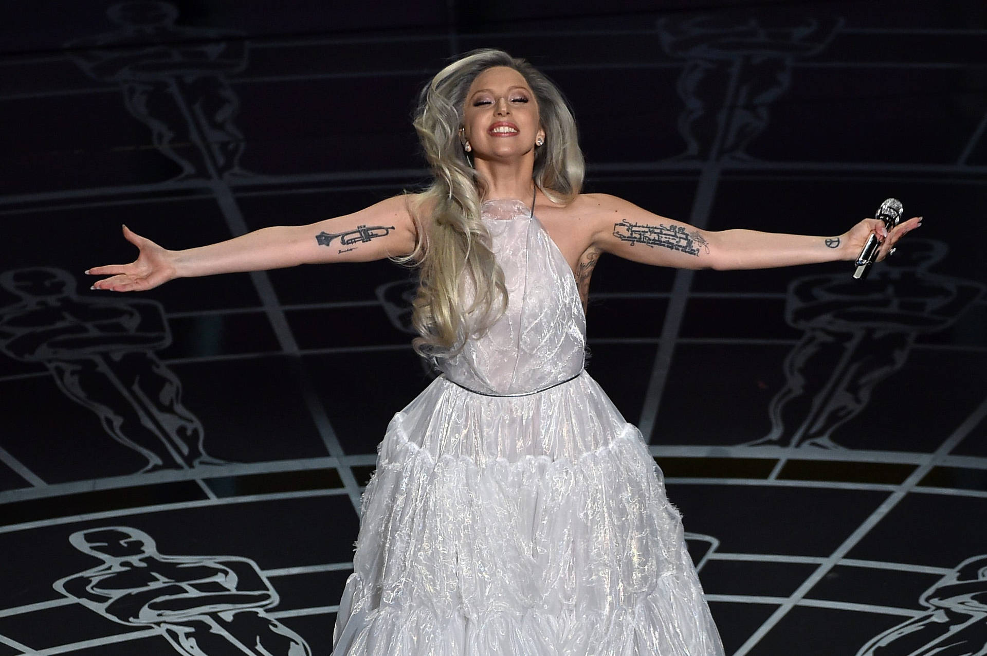 Lady Gaga 身穿白色長袍在舞台上表演，雙臂伸展。