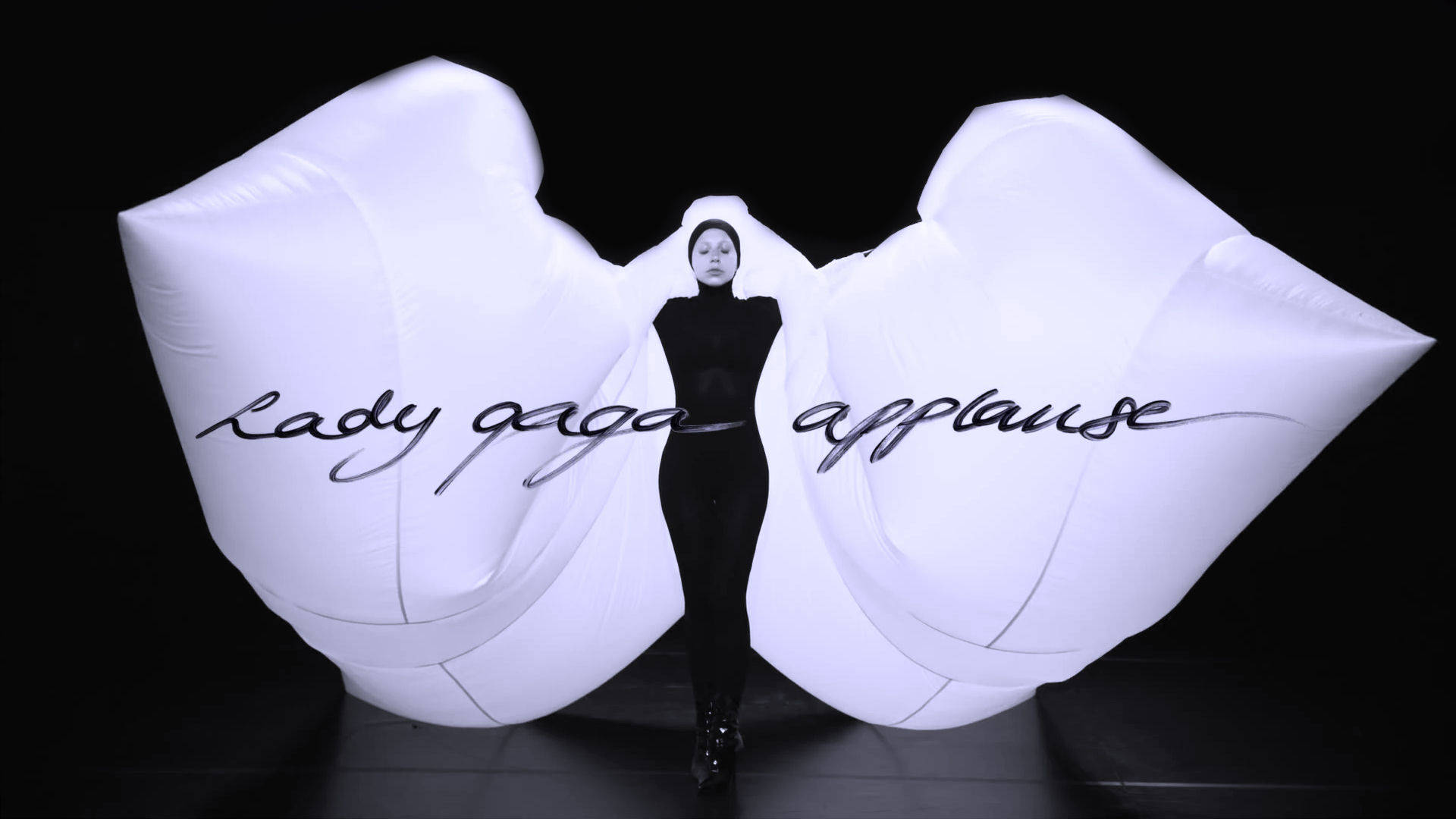 Lady Gaga 身穿黑色緊身連衣褲，巨大的白色充氣手拼出她的名字。