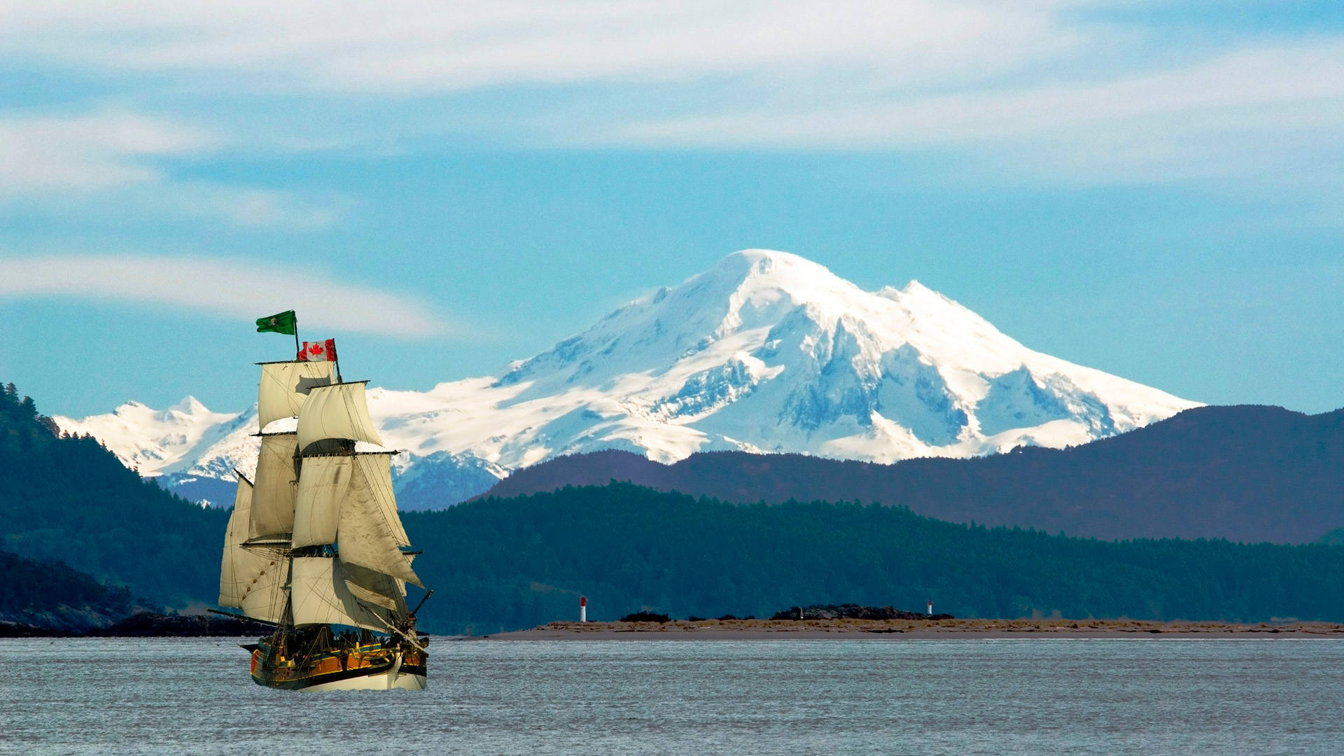 「Lady Washington」帆船 壁紙 — 一艘高大的帆船在平靜如鏡的海面上航行，雄偉的雪山在森林覆蓋的山丘後方升起，天空清澈湛藍。