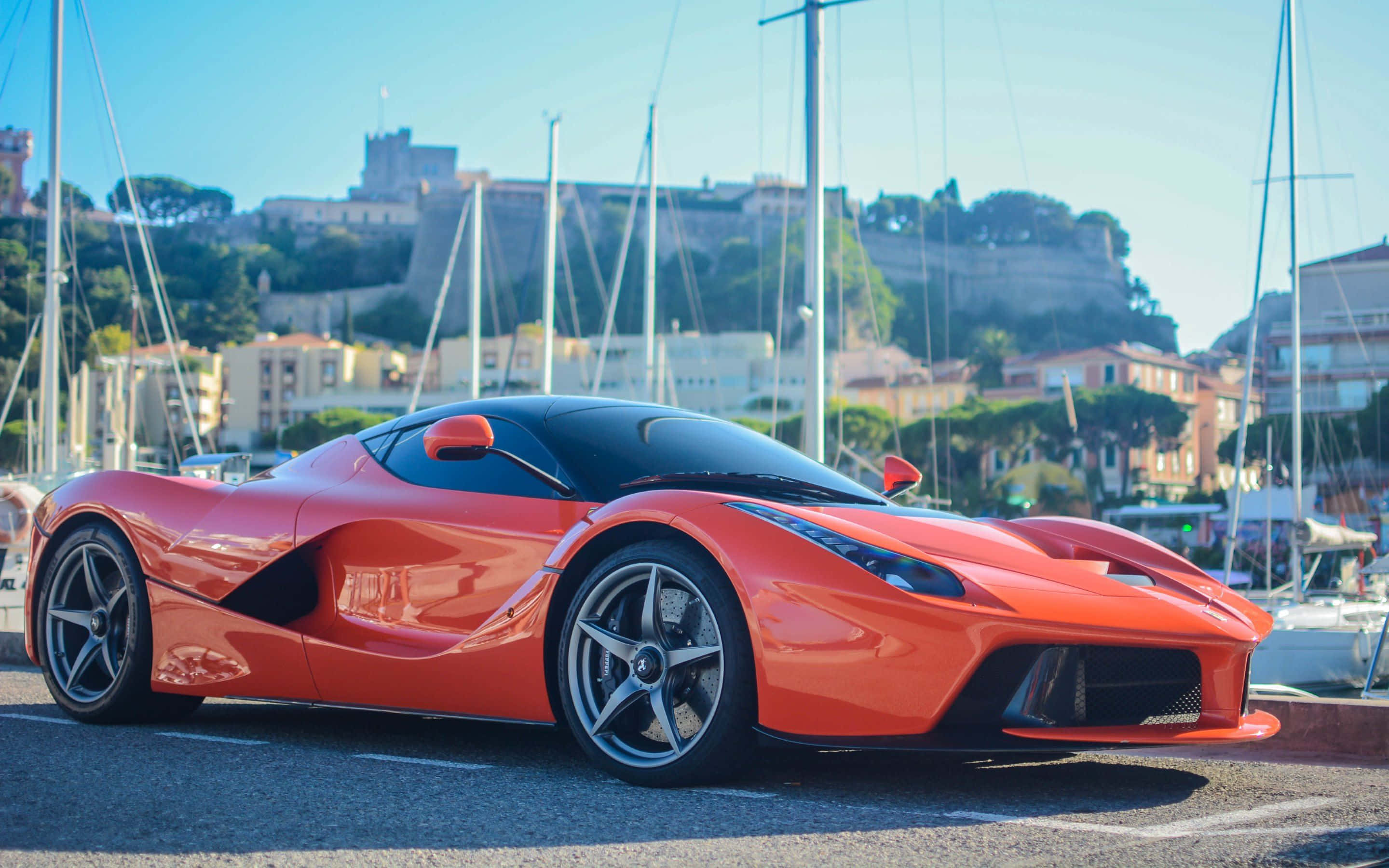 法拉利LaFerrari：力量與優雅的結合 壁紙 — 一輛鮮豔的橙色LaFerrari超級跑車在明亮的陽光下閃閃發光，停泊在一個遊艇碼頭，背景有帆船和歷史建築。