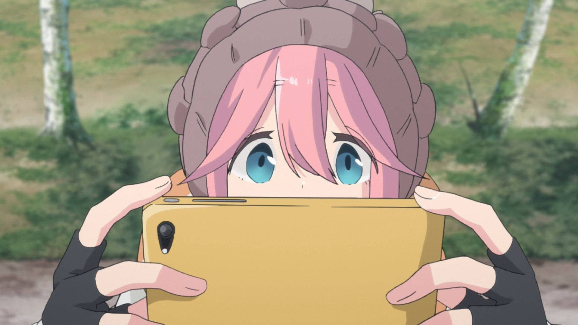 《Laid Back Camp》奈奈子手持手機 壁紙 — 粉紅色頭髮的動漫女孩戴著辮子帽，在森林中用黃色手機自拍。