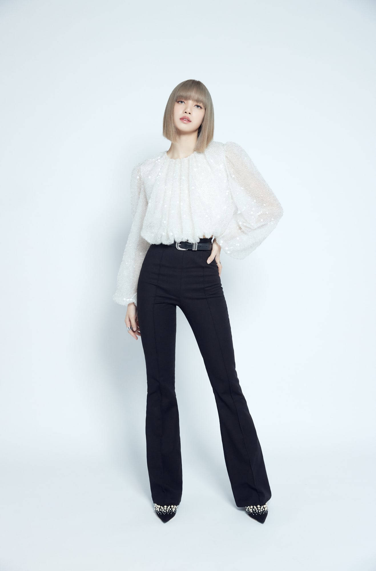 Lalisa Manoban 肖像照 壁紙 — 一位身穿白色質感襯衫和黑色喇叭褲的女性在純白背景前自信地擺姿勢。