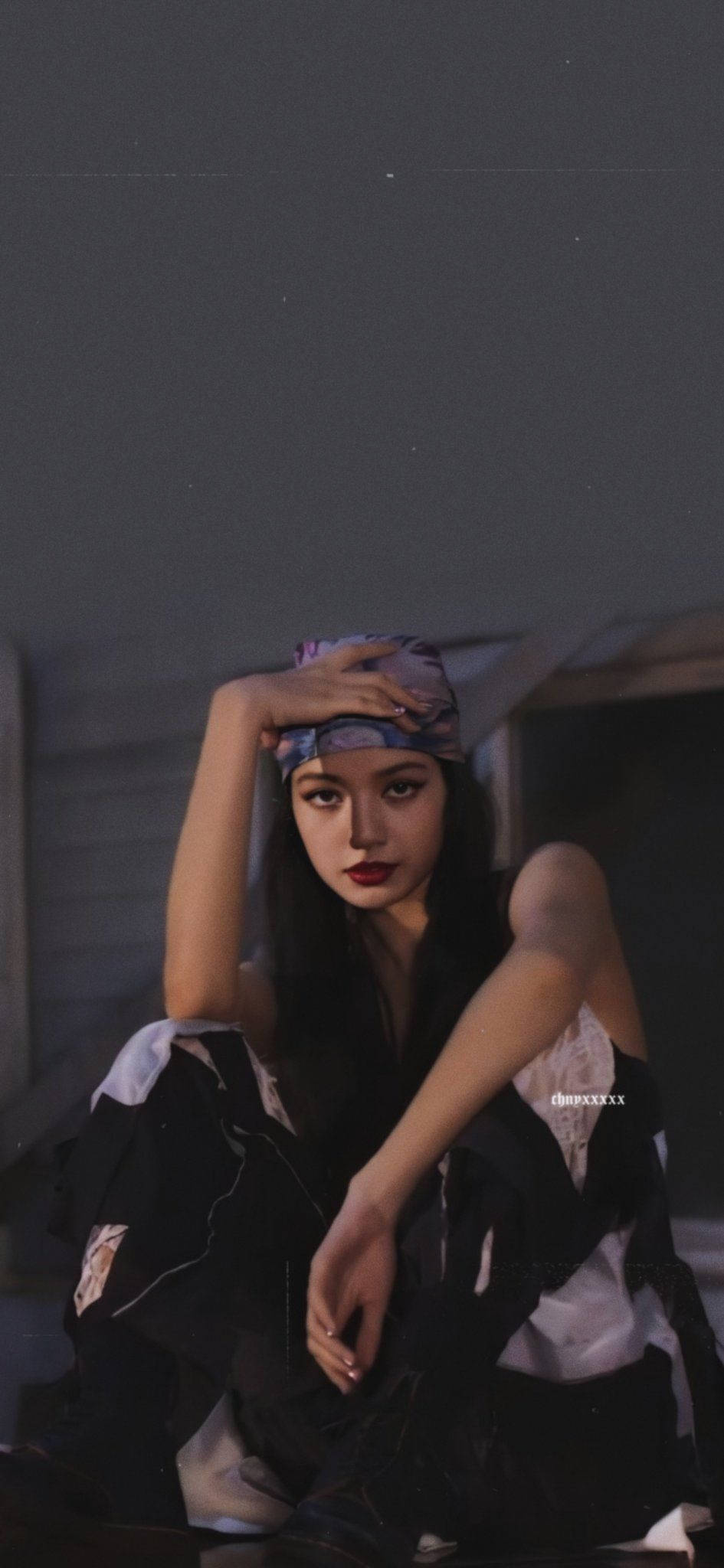 Lalisa Manoban《City Girls》表演片段 壁紙 — 一位年輕女性，深色頭髮，大膽紅唇，坐在昏暗的房間裡，戴著圖案頭巾，穿著黑白服裝，手放在額頭上。