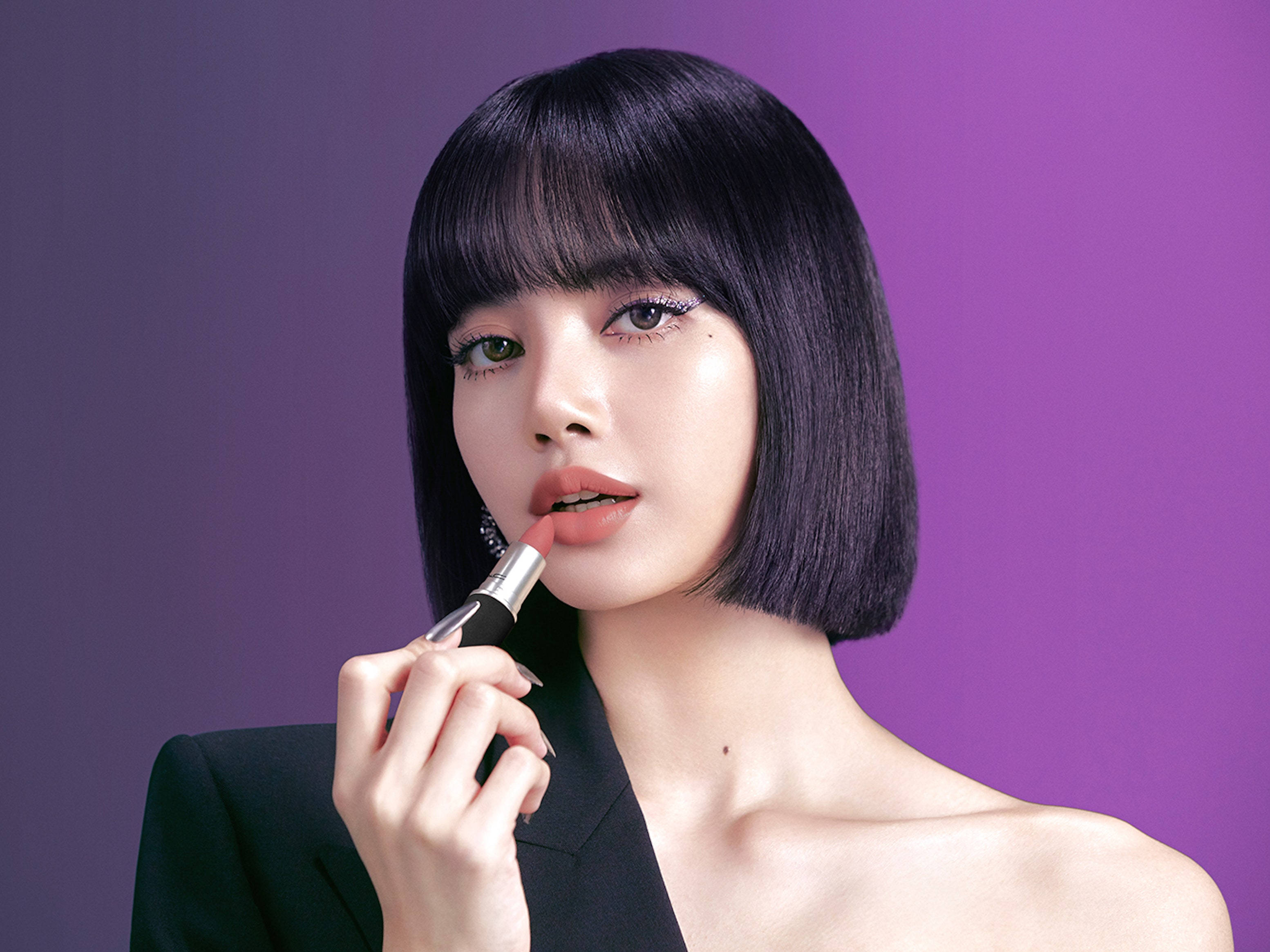 Lalisa Manoban 為 MAC 拍攝 壁紙 — 一位擁有光滑黑色鮑伯頭和大膽眼線的女性，在漸變紫色背景下塗抹珊瑚色唇膏。