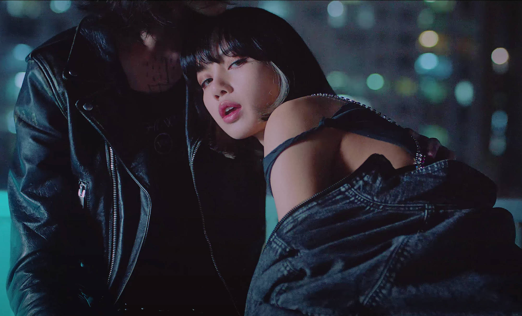 Lalisa Manoban 與 LOREN 壁紙 — 一位身穿牛仔外套和黑色上衣的女性在夜晚的霓虹城市燈光下靠著一位身穿皮夾克的男性。
