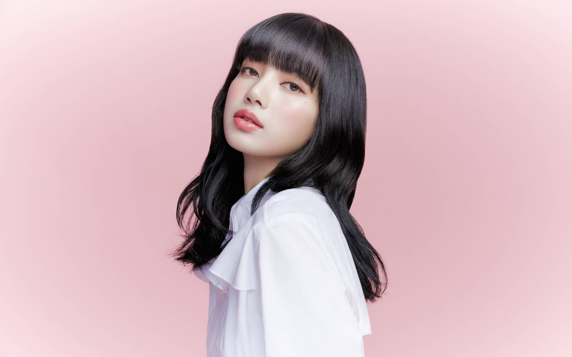 Lalisa Manoban 黑髮波浪造型 壁紙 — 一位年輕女性，長長的黑髮和劉海，穿著白色襯衫，背景是柔和的粉紅色。