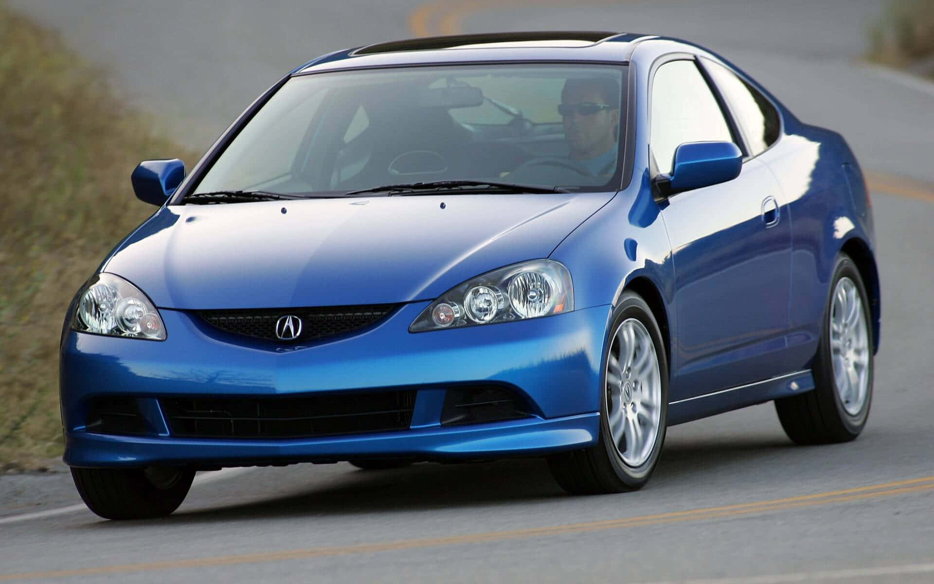 Acura Rsx 桌布 壁紙 — 一輛充滿活力的藍色Acura RSX雙門跑車在陽光明媚的道路上行駛，透過擋風玻璃可以看到司機。