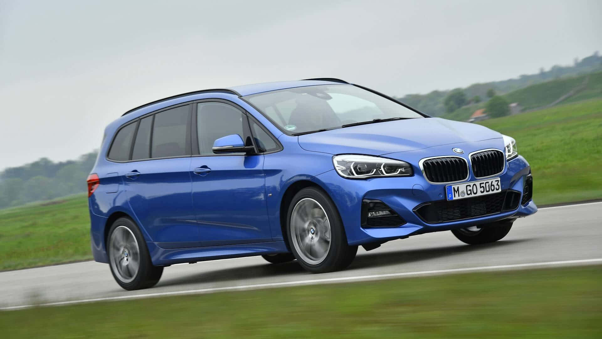 Bmw 2 Series 桌布 壁紙 — 一輛充滿活力的藍色BMW旅行車在鄉村道路上疾馳，背景是模糊的綠色田野和陰天。