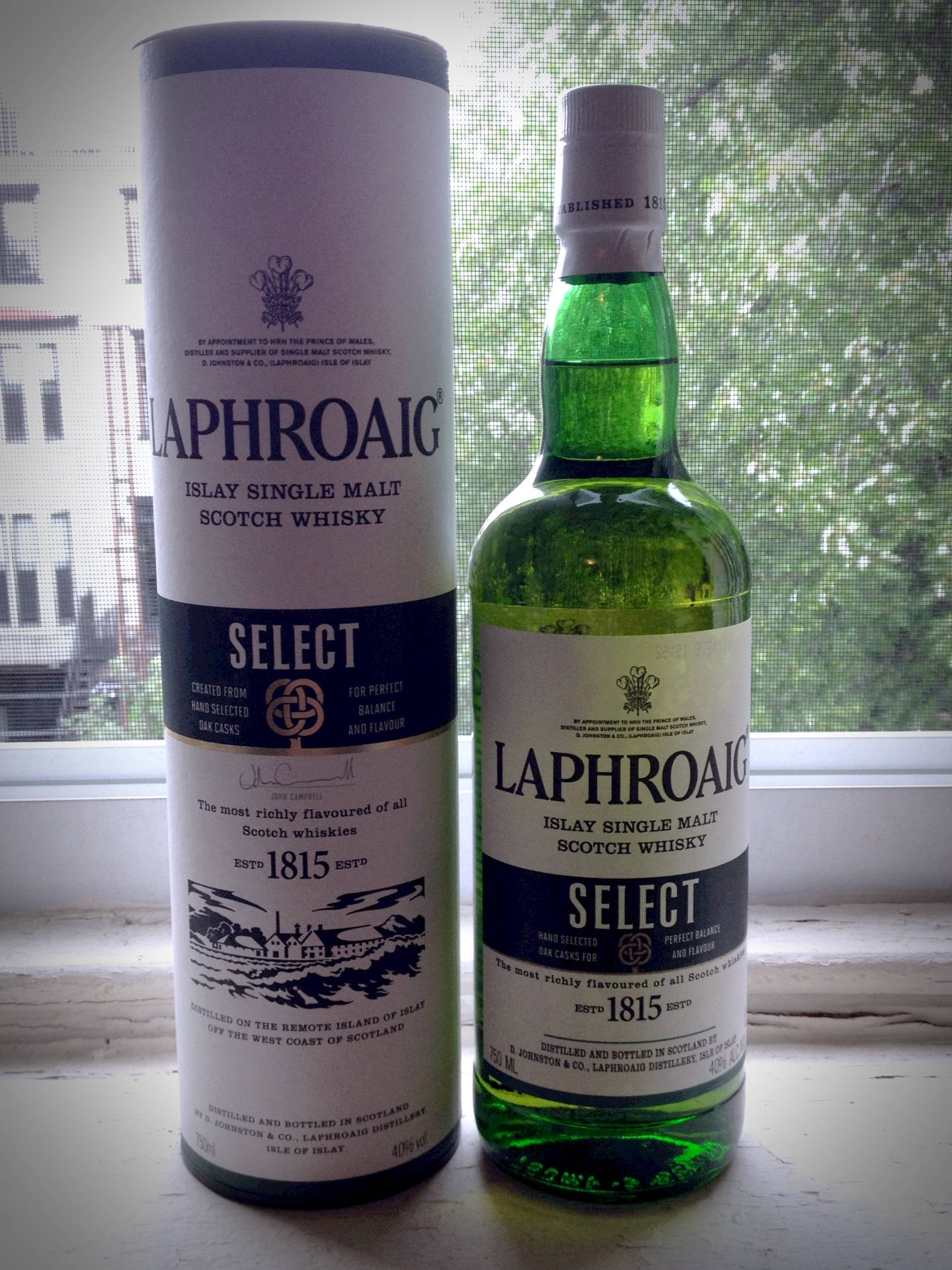 Laphroaig Select威士忌酒瓶和盒子喺窗台上，有城市景觀。
