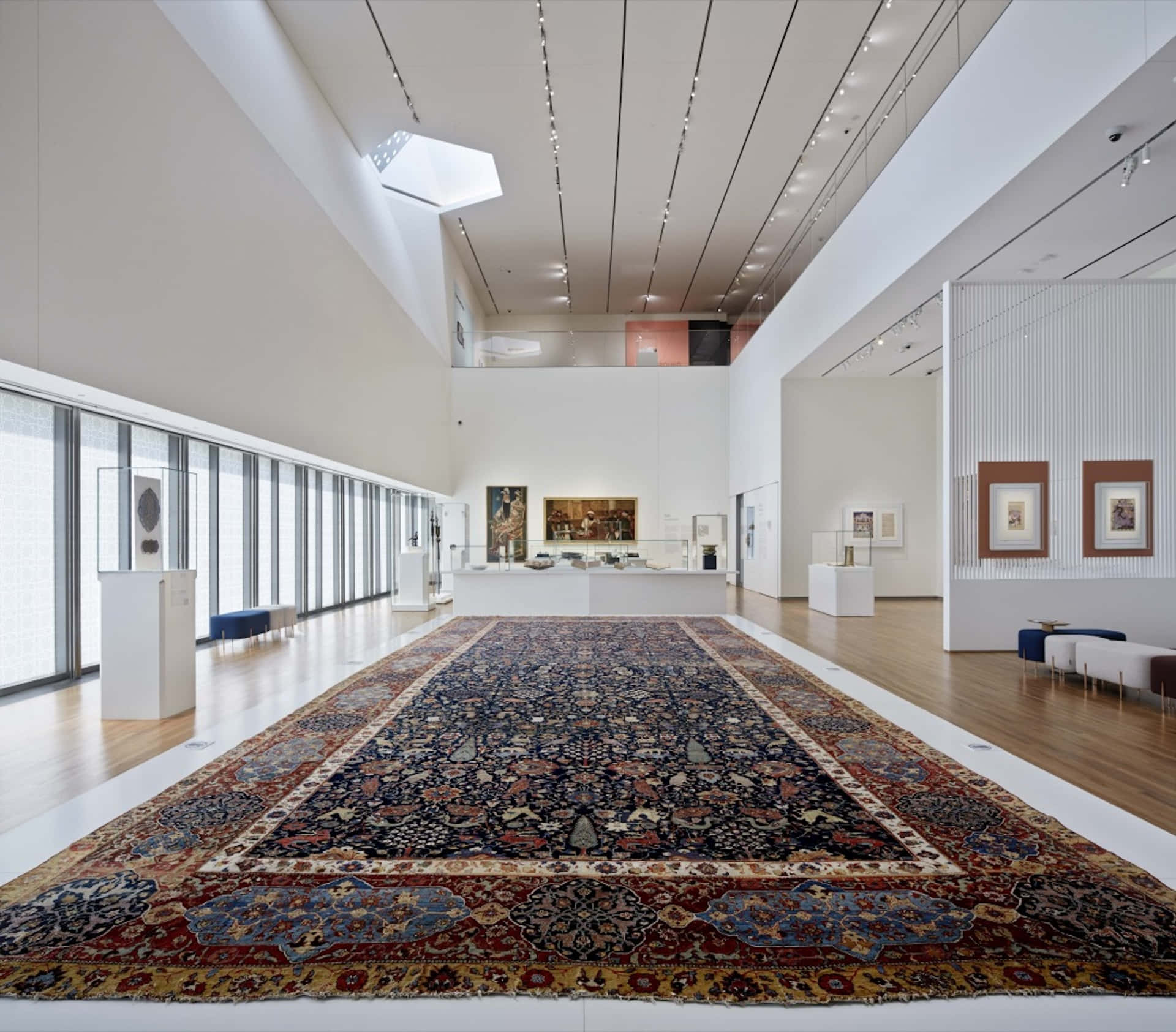 Aga Khan Museum 桌布 壁紙 — 一個大型華麗波斯地毯主導著一個極簡現代藝術畫廊，擁有白色牆壁和木地板。