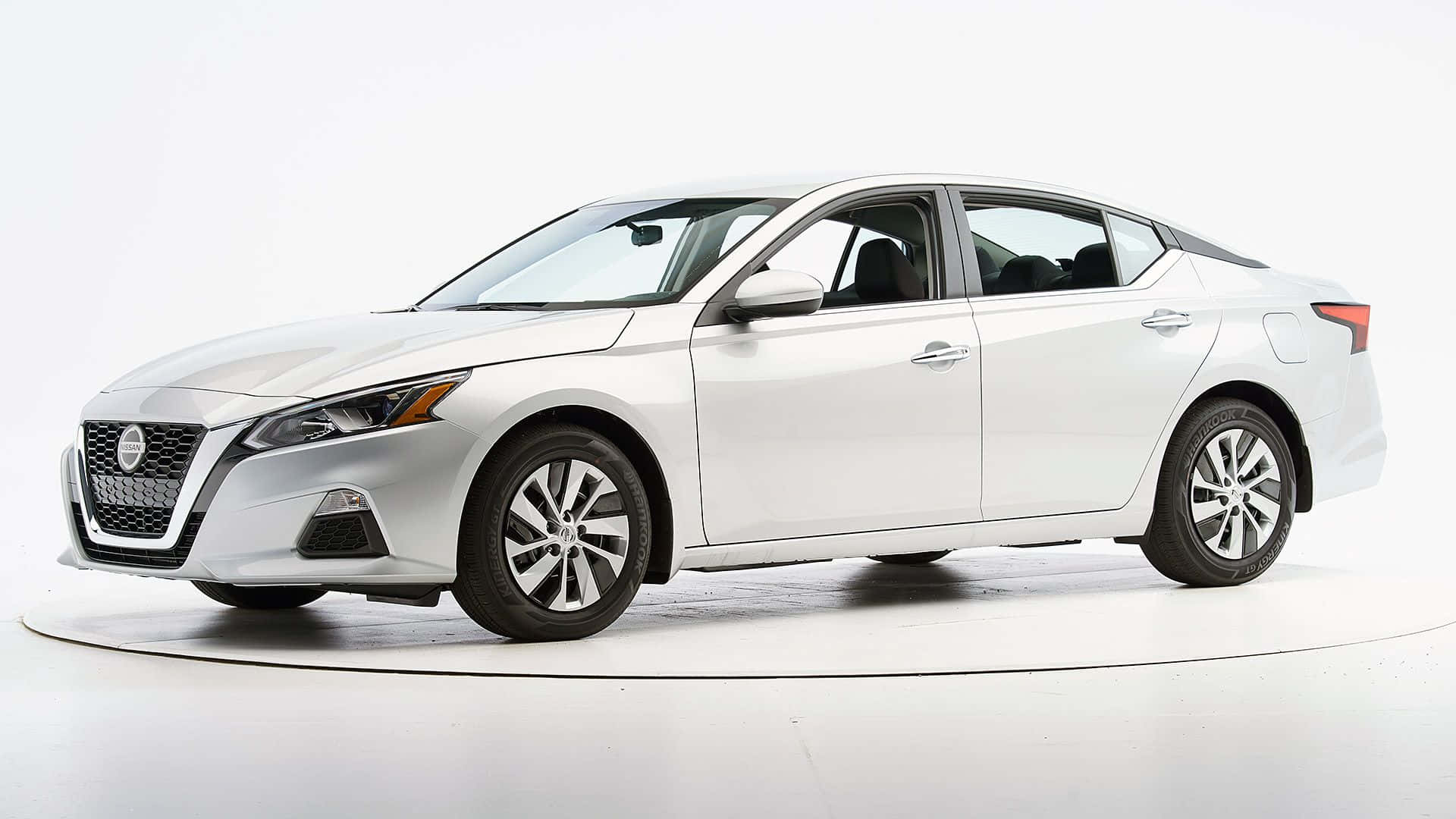 Nissan Altima 桌布 壁紙 — 一輛流線型白色日產房車在乾淨的攝影棚中展示，配有柔和燈光和簡約白色地板。